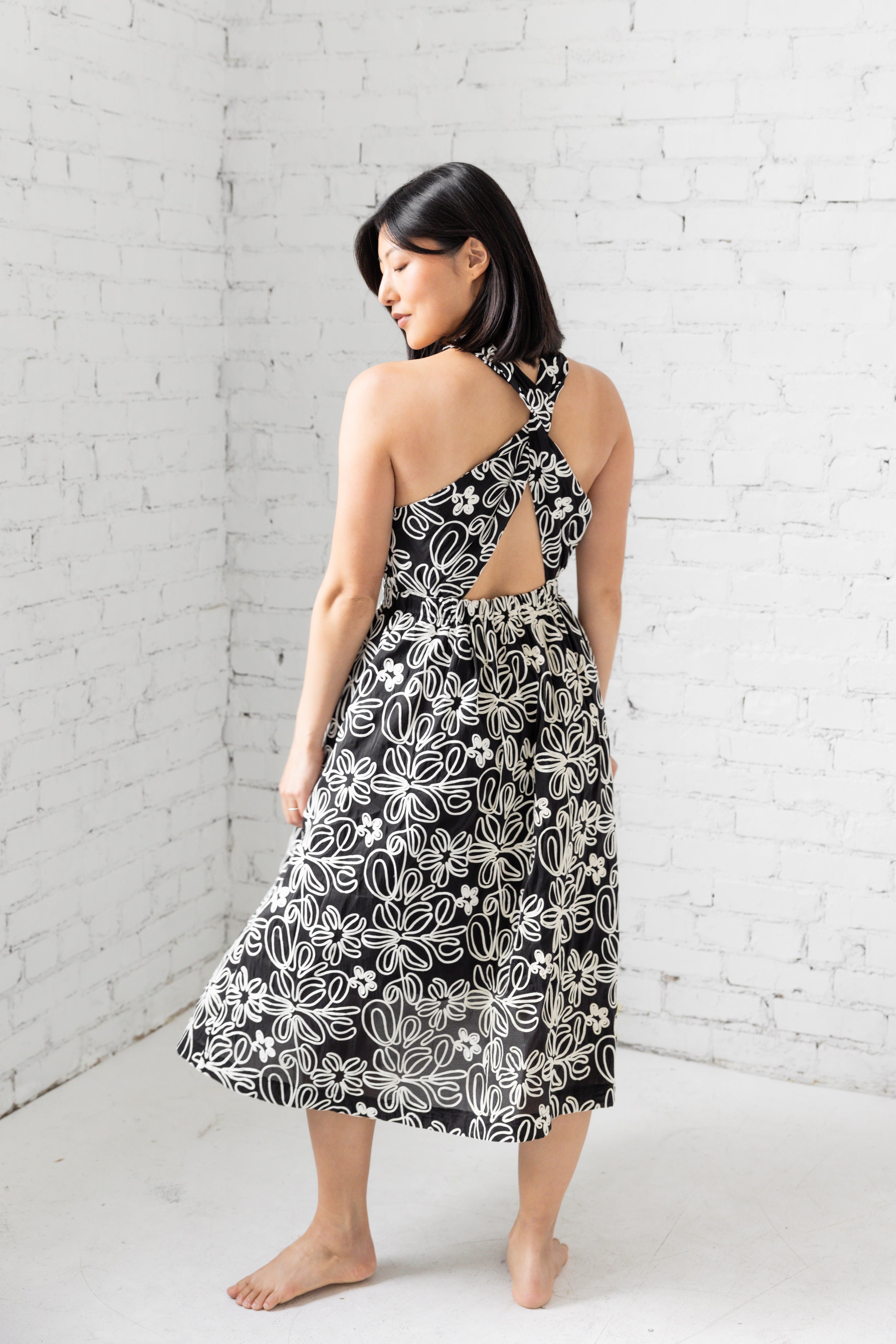 Model is wearing halter neckline midi dress with black and white floral design.