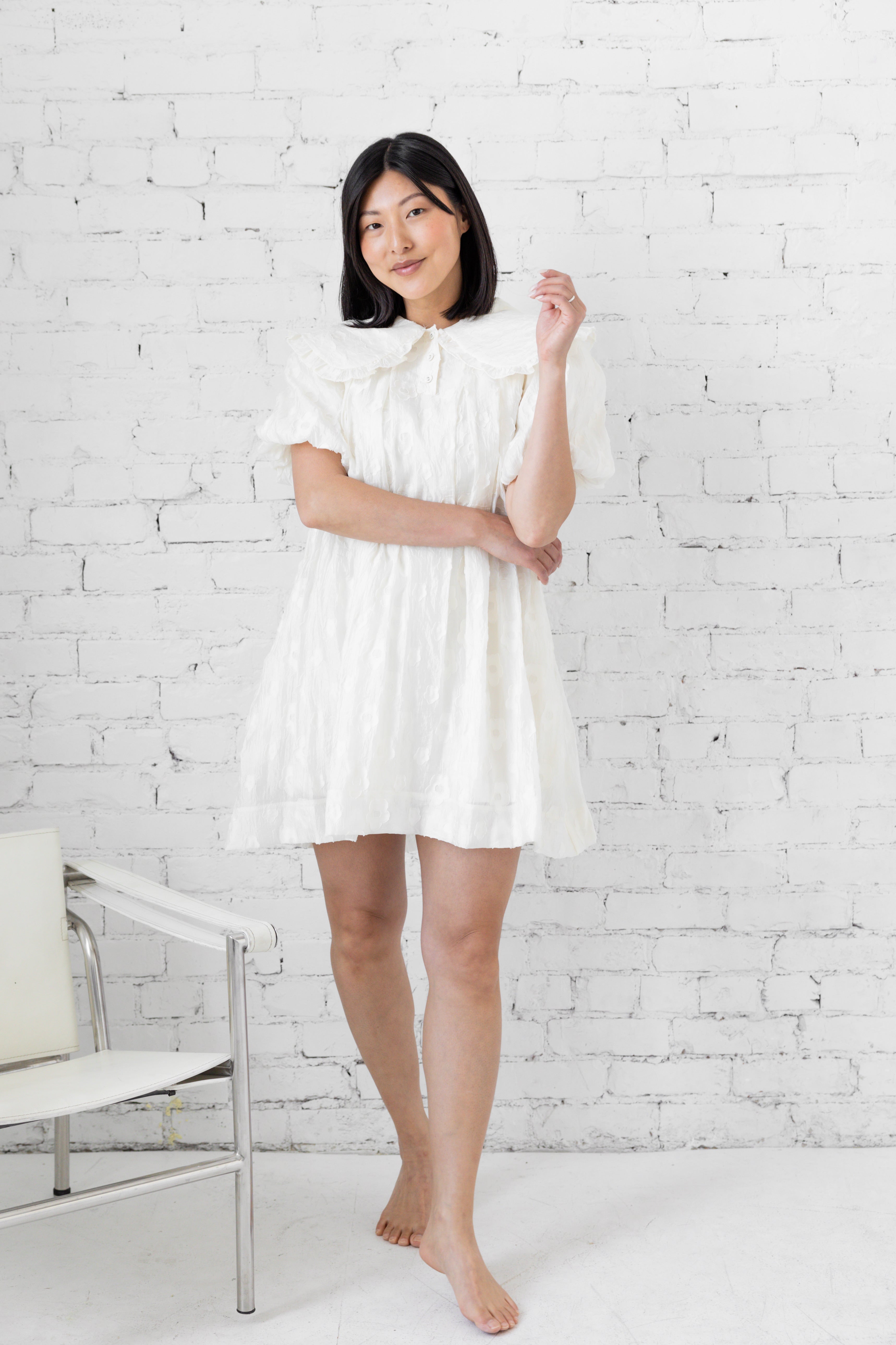 Model wearing white mini dress with puffer sleeves and peter pan collar.