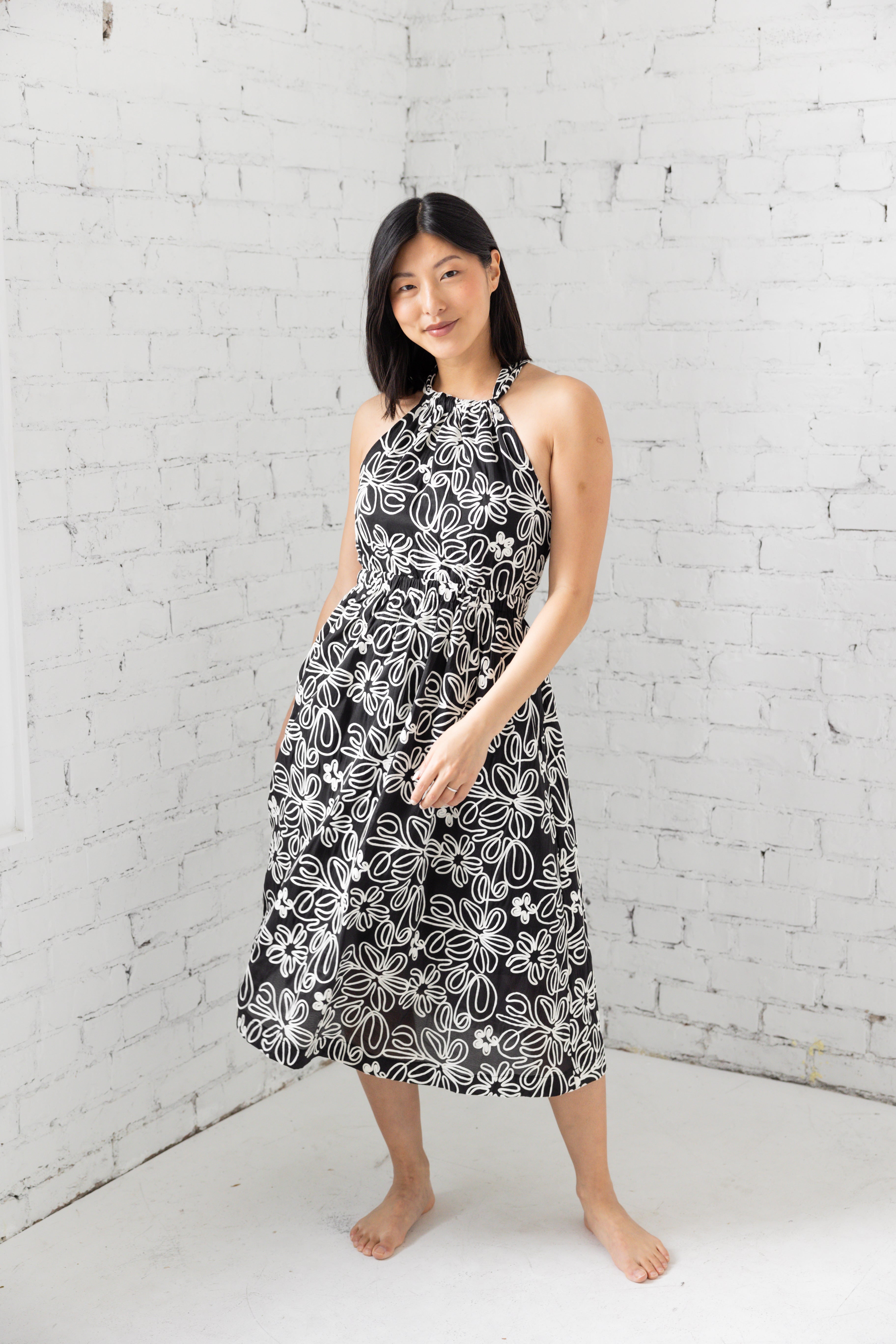 Model is wearing halter neckline midi dress with black and white floral design.