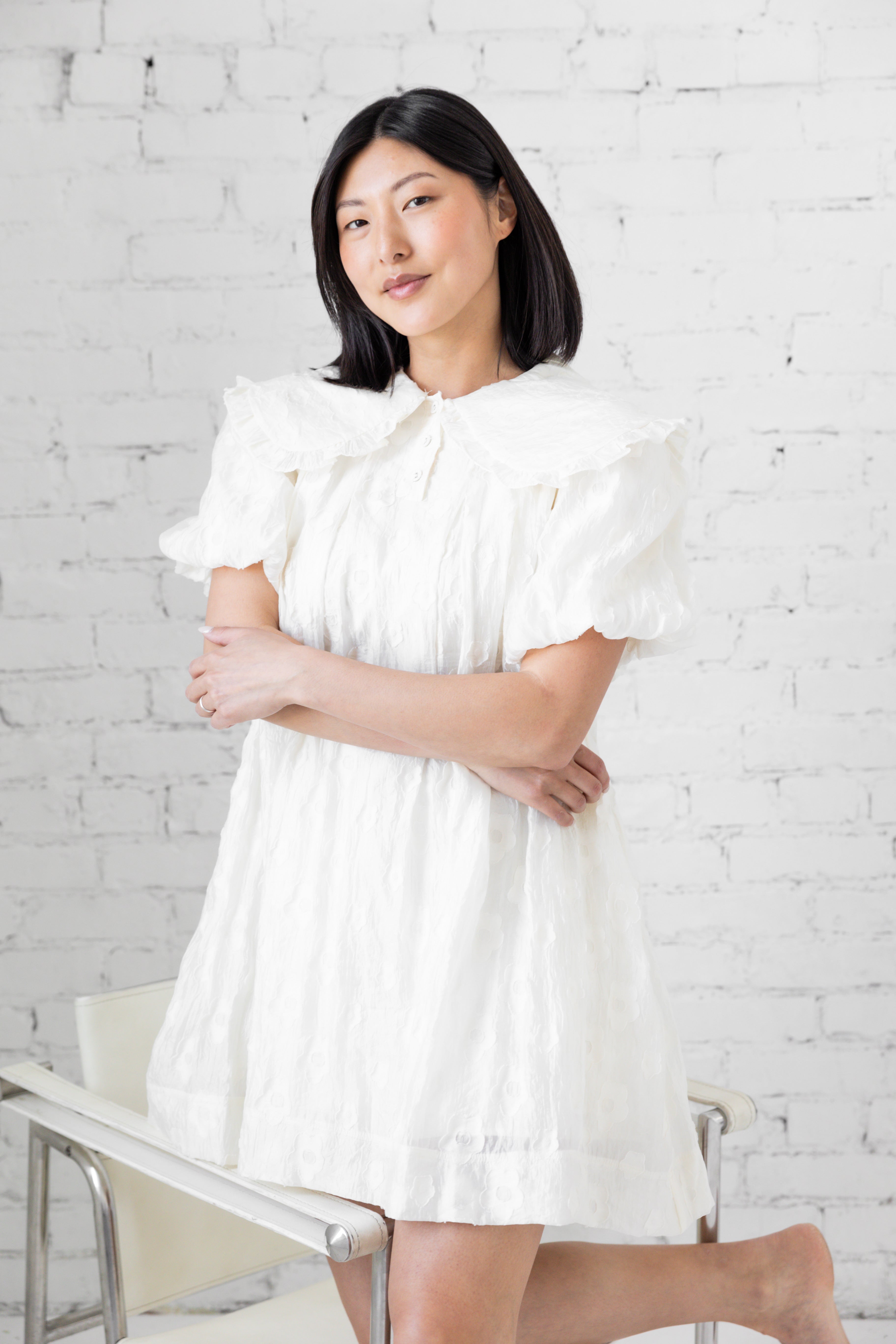 Model wearing white mini dress with puffer sleeves and peter pan collar.