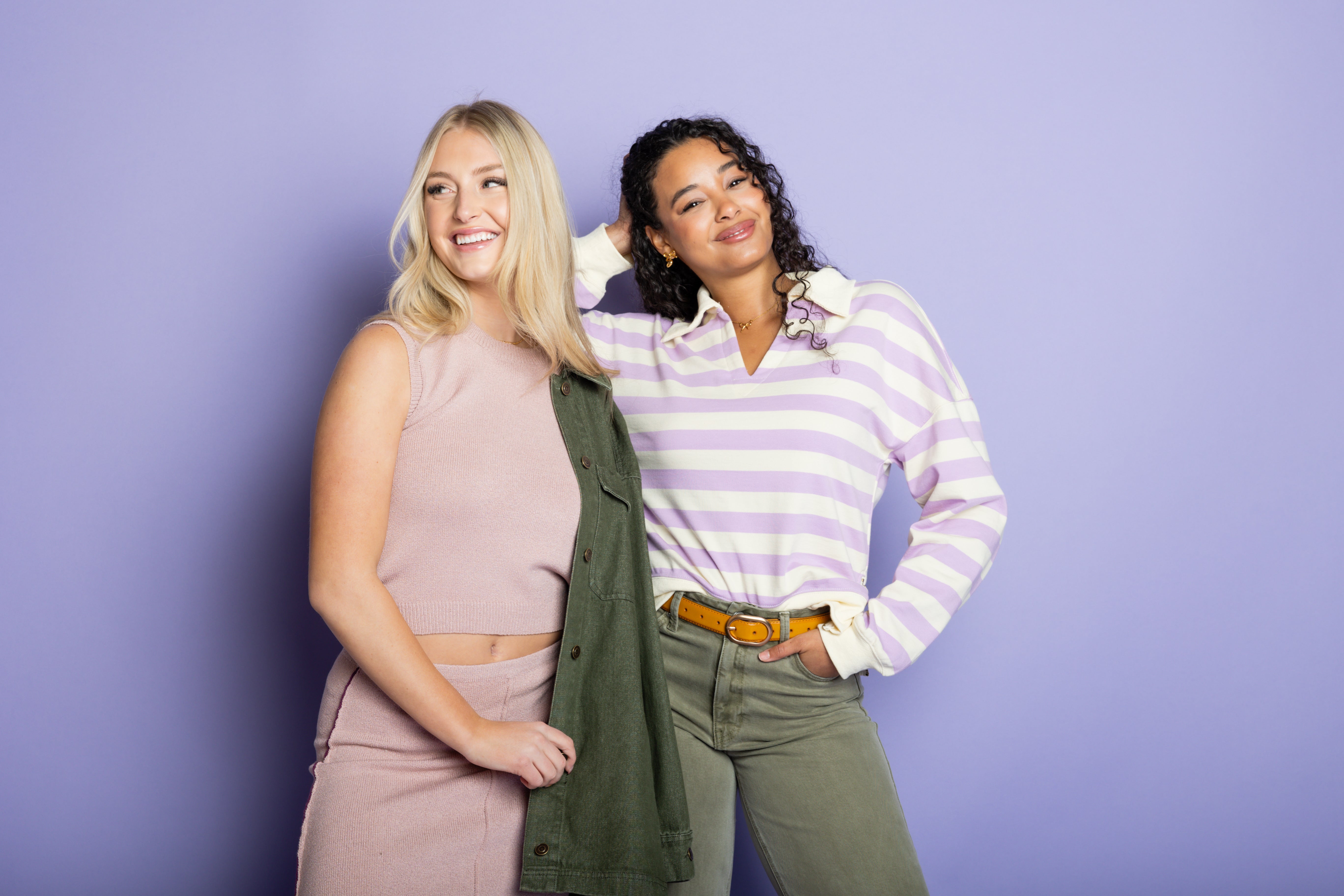 Two models wearing purple colorful outfits with a purple backdrop.