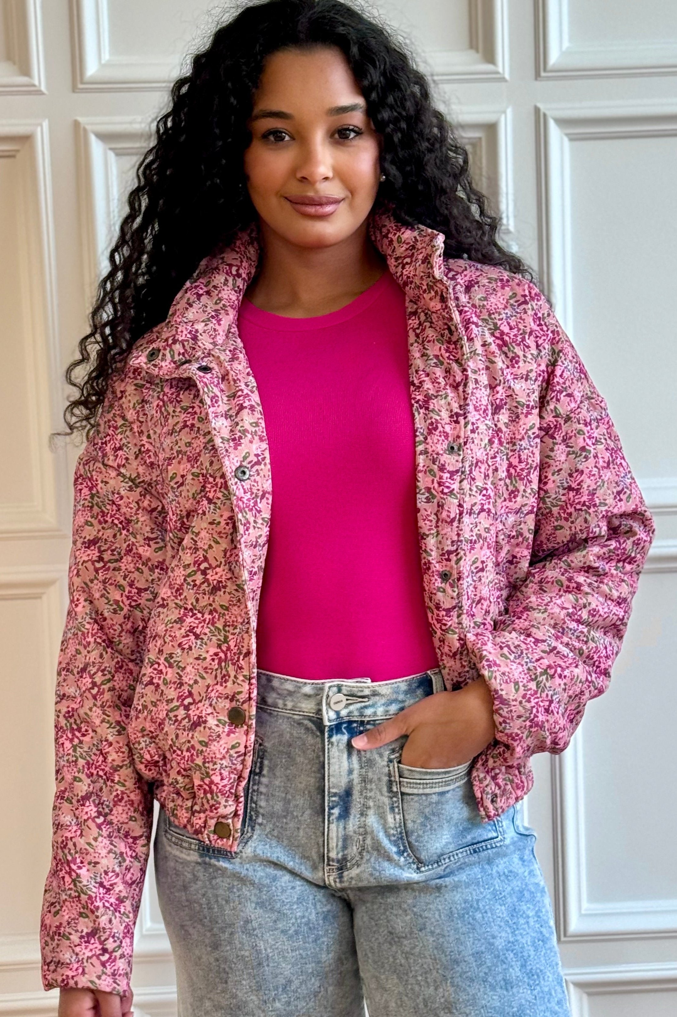 Woman standing wearing pink jacket, tank, and light wash jeans. 