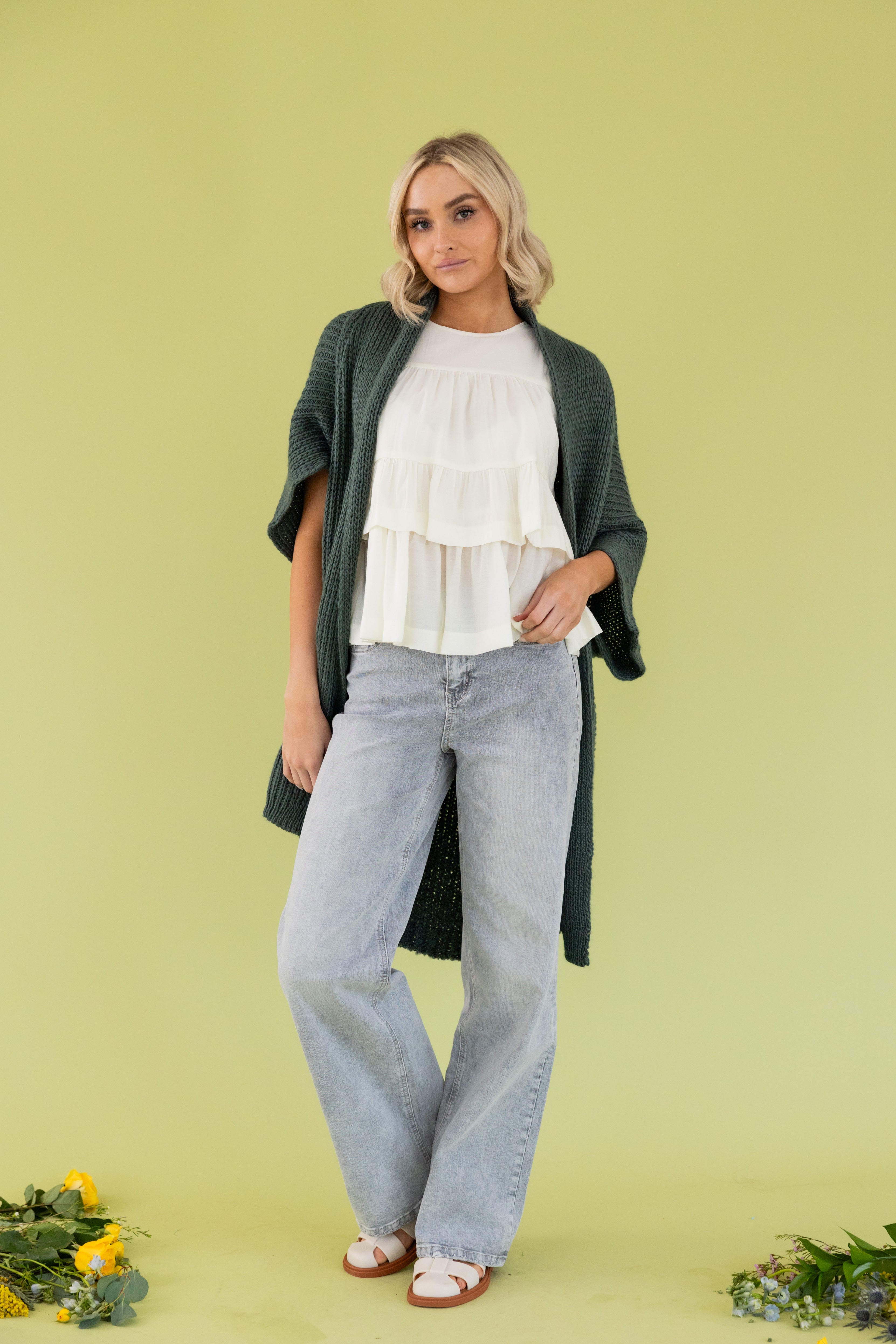 Model is wearing green cardigan in white blouse and grey jeans. 