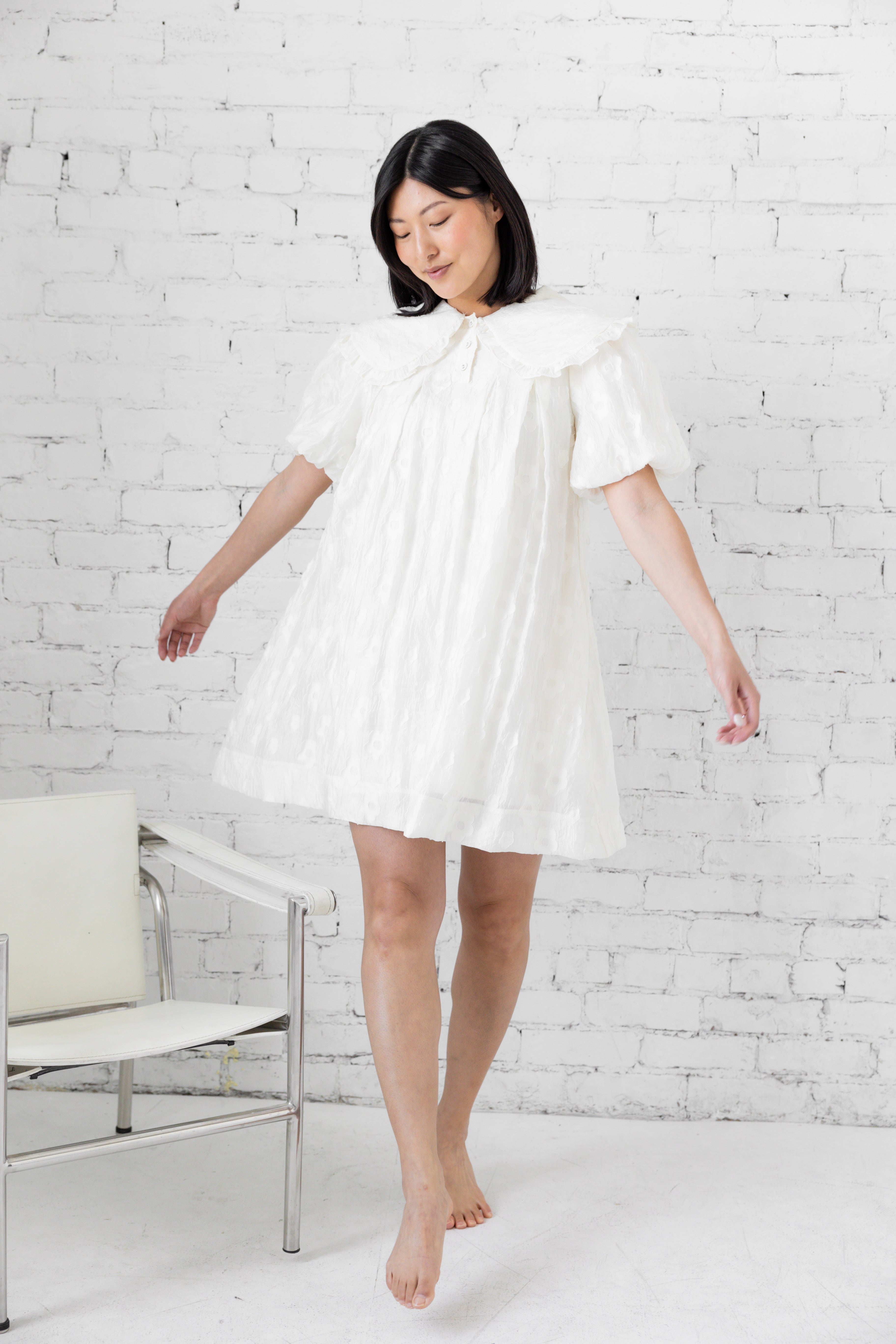 Model wearing white mini dress with puffer sleeves and peter pan collar.