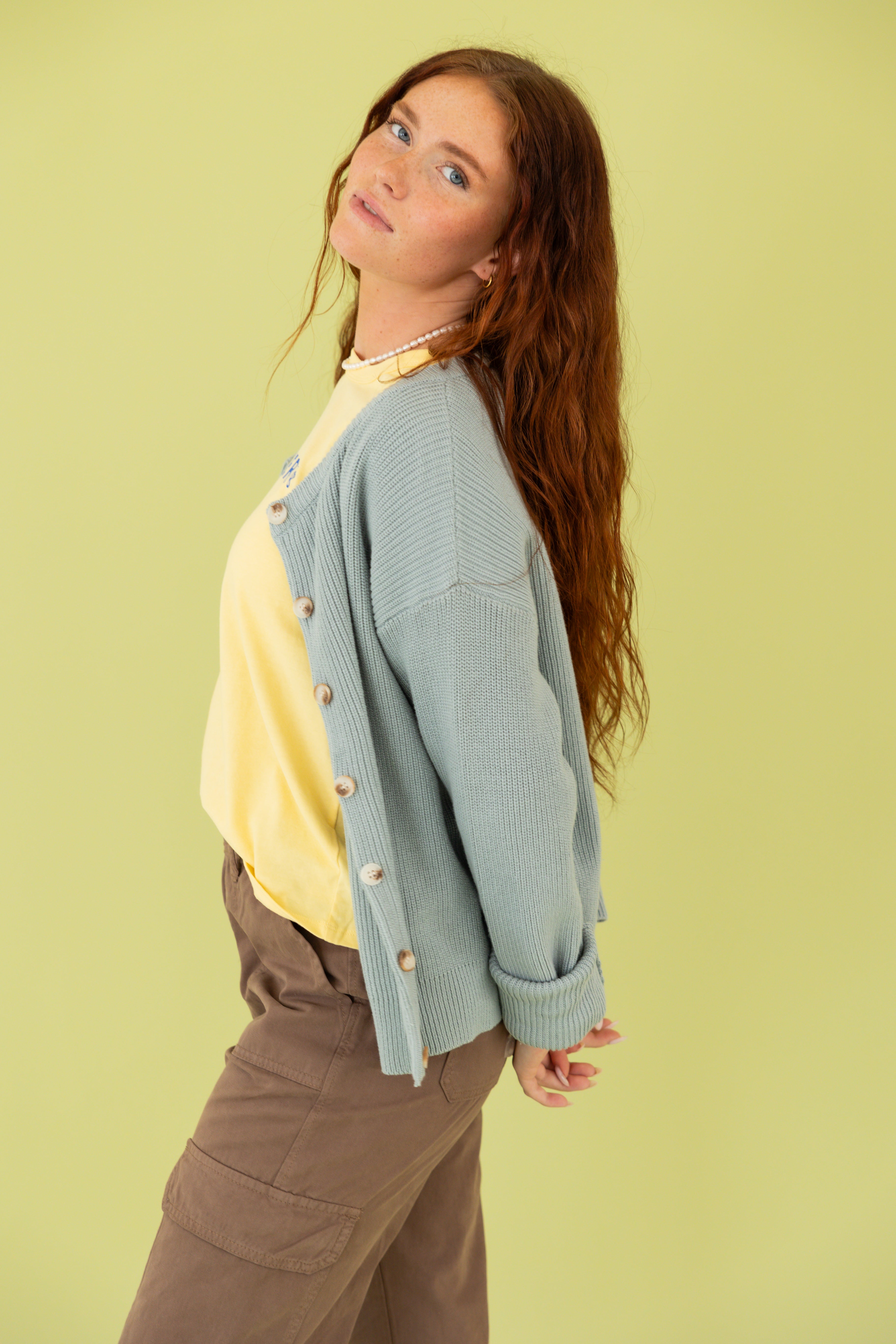 Model is wearing a blue cardigan and brown pants.