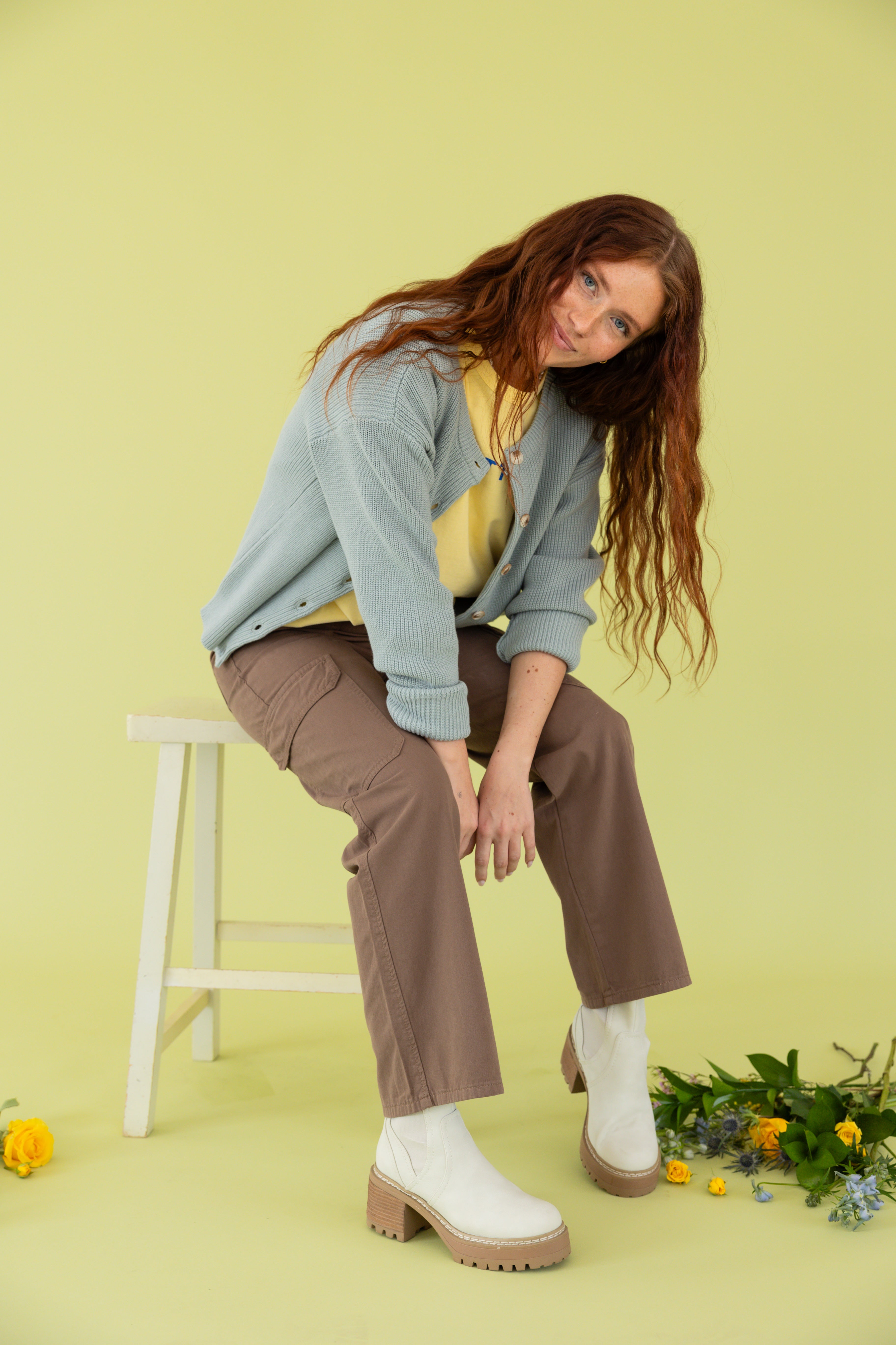 Model is wearing a blue cardigan and brown pants.