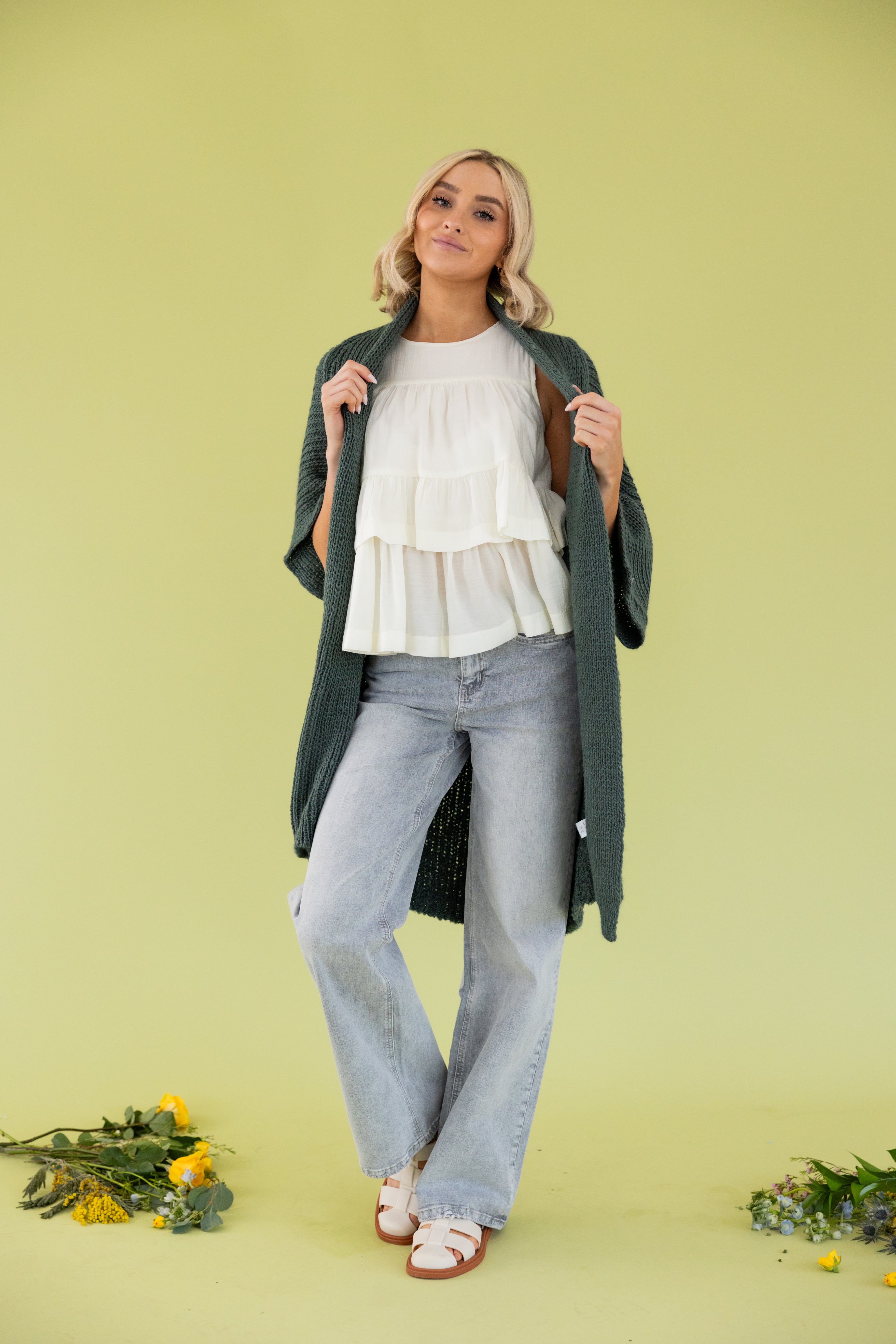 Model is wearing green cardigan in white blouse and grey jeans. 