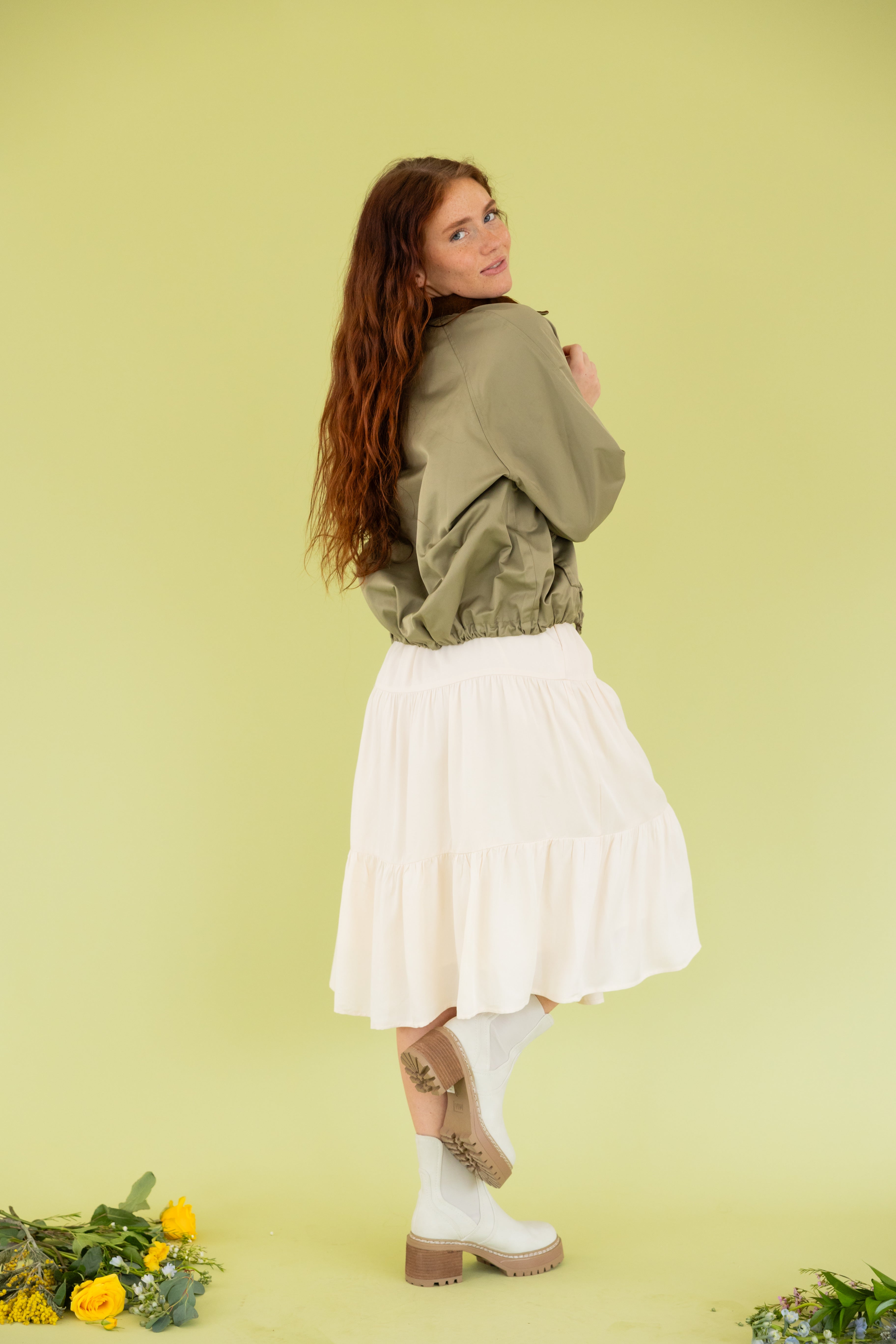 Model is wearing a green bomber jacket and midi dress.