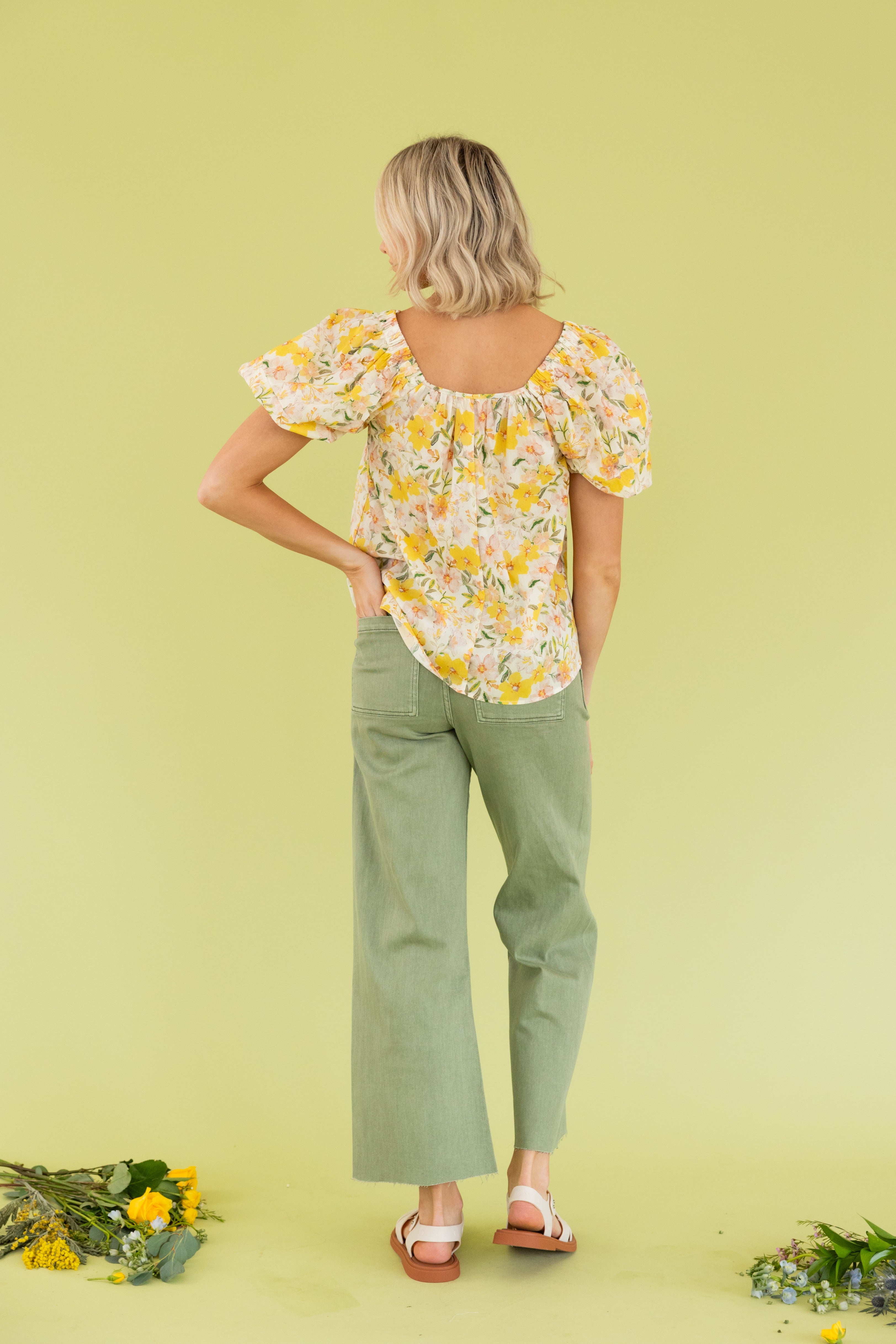 Model is wearing a yellow floral blouse and green wide leg pant.  