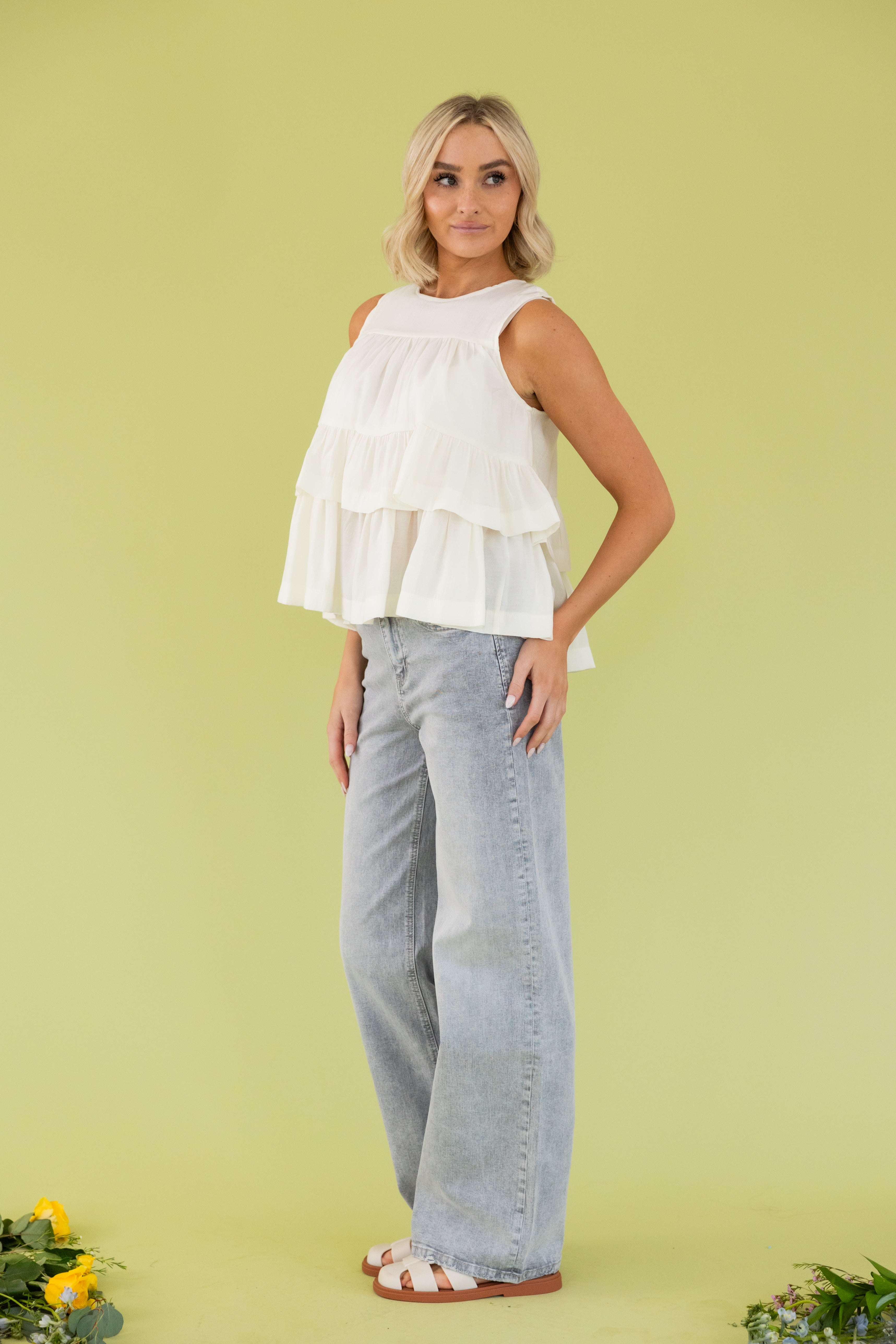 Model is wearing a white blouse and grey straight leg pant. 