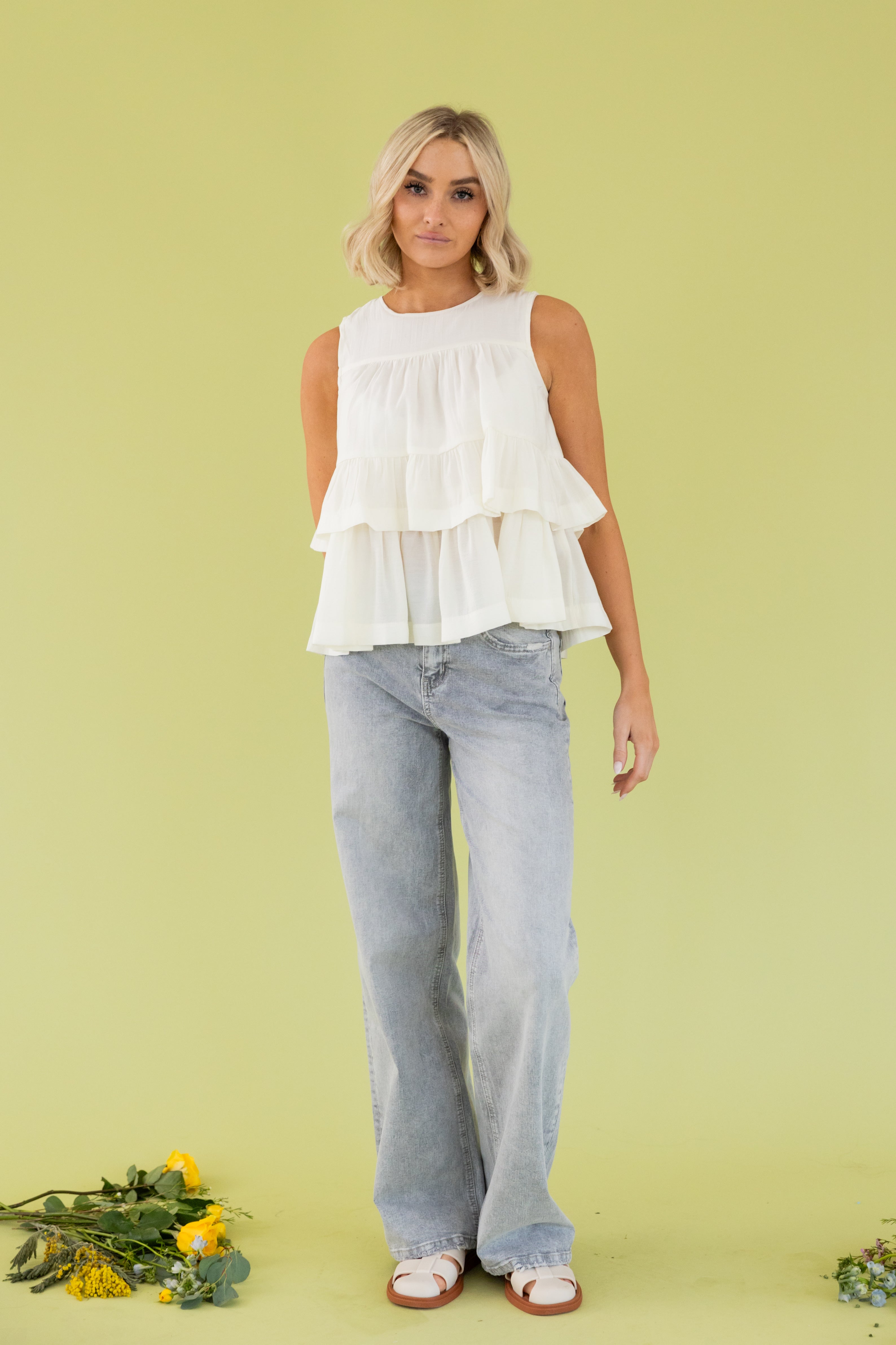 Model is wearing a white blouse and grey straight leg pant. 