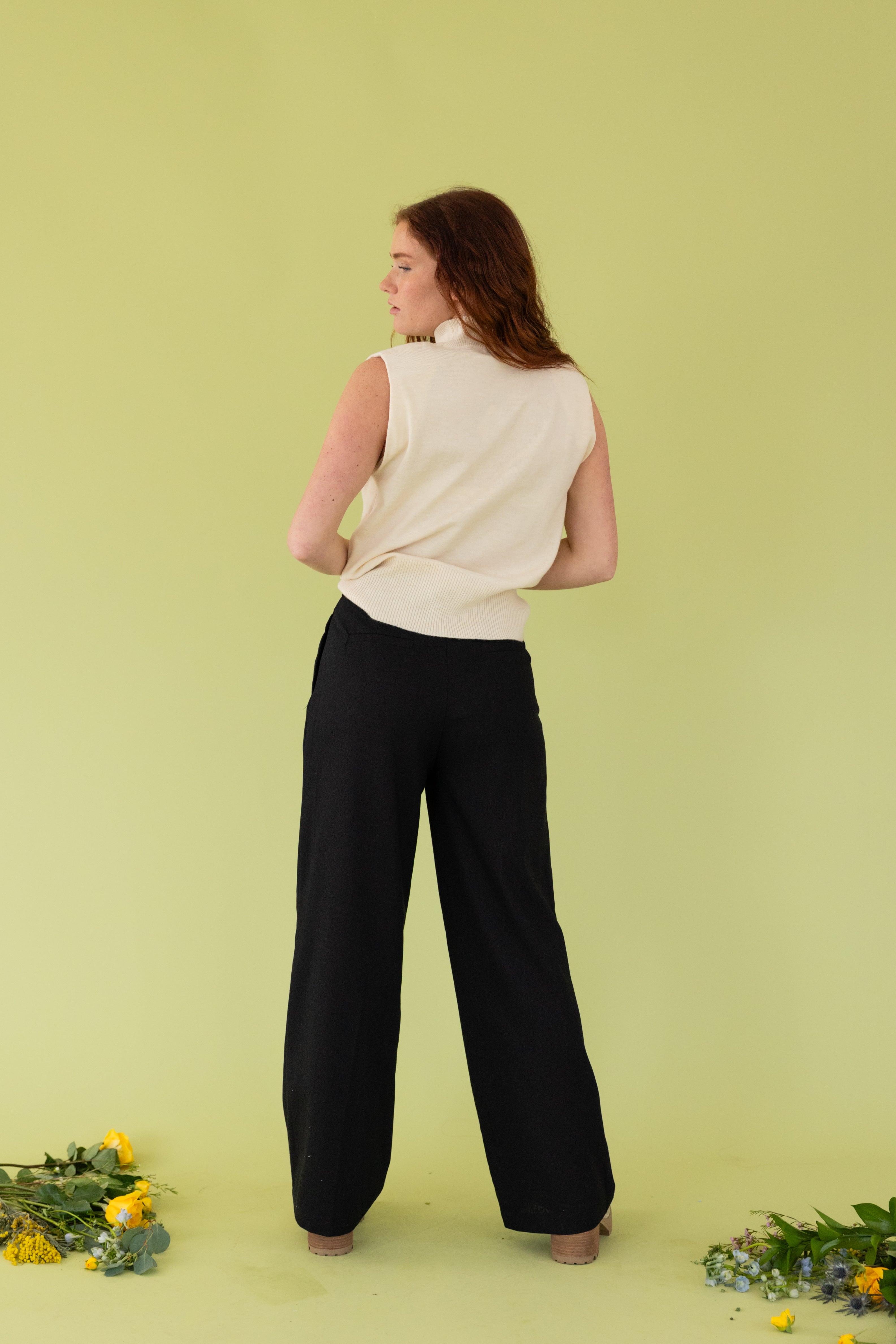 Model is wearing white sweater top and high waisted black slacks. 