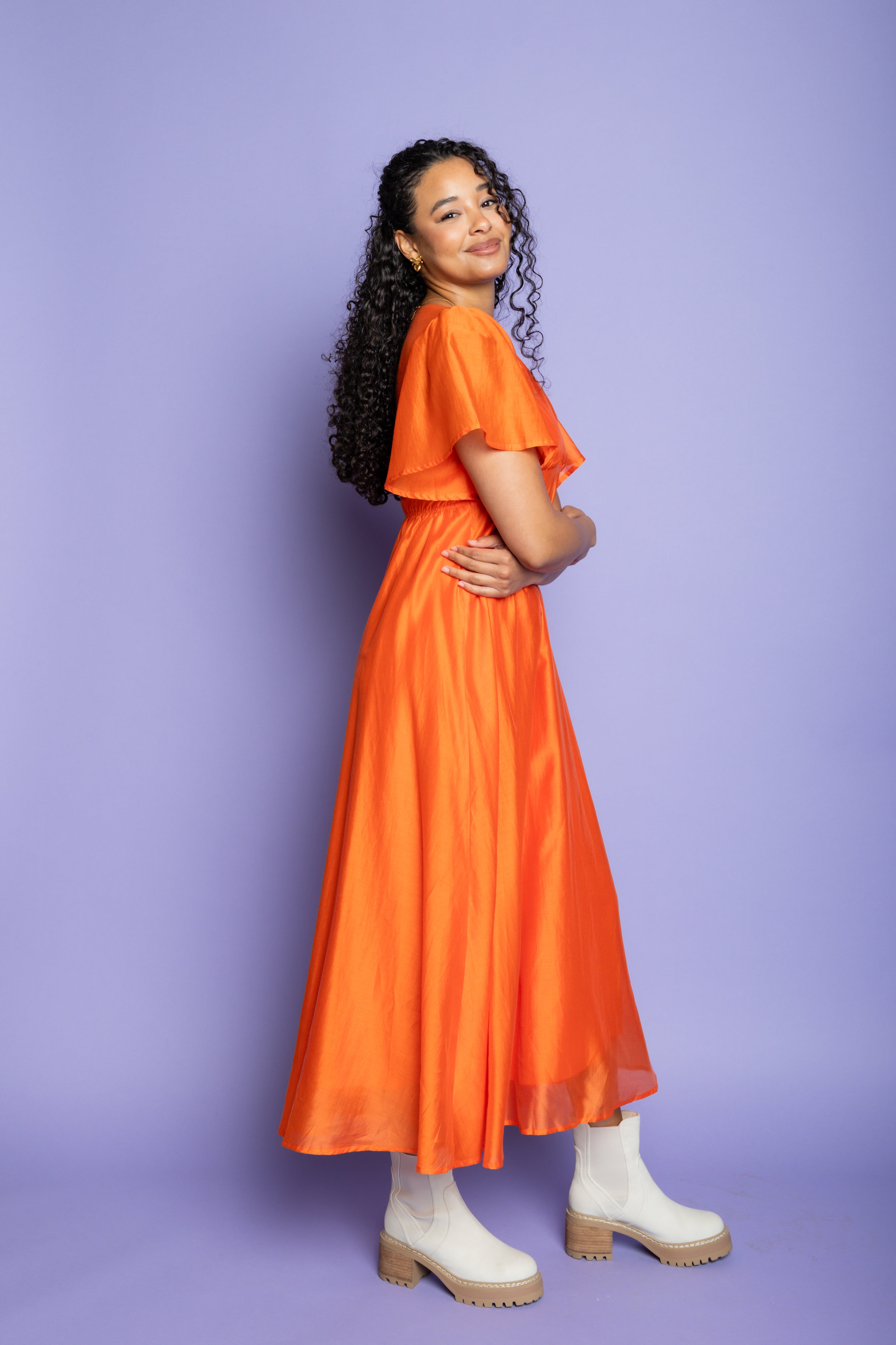 Model in a photoshoot wearing an orange midi dress