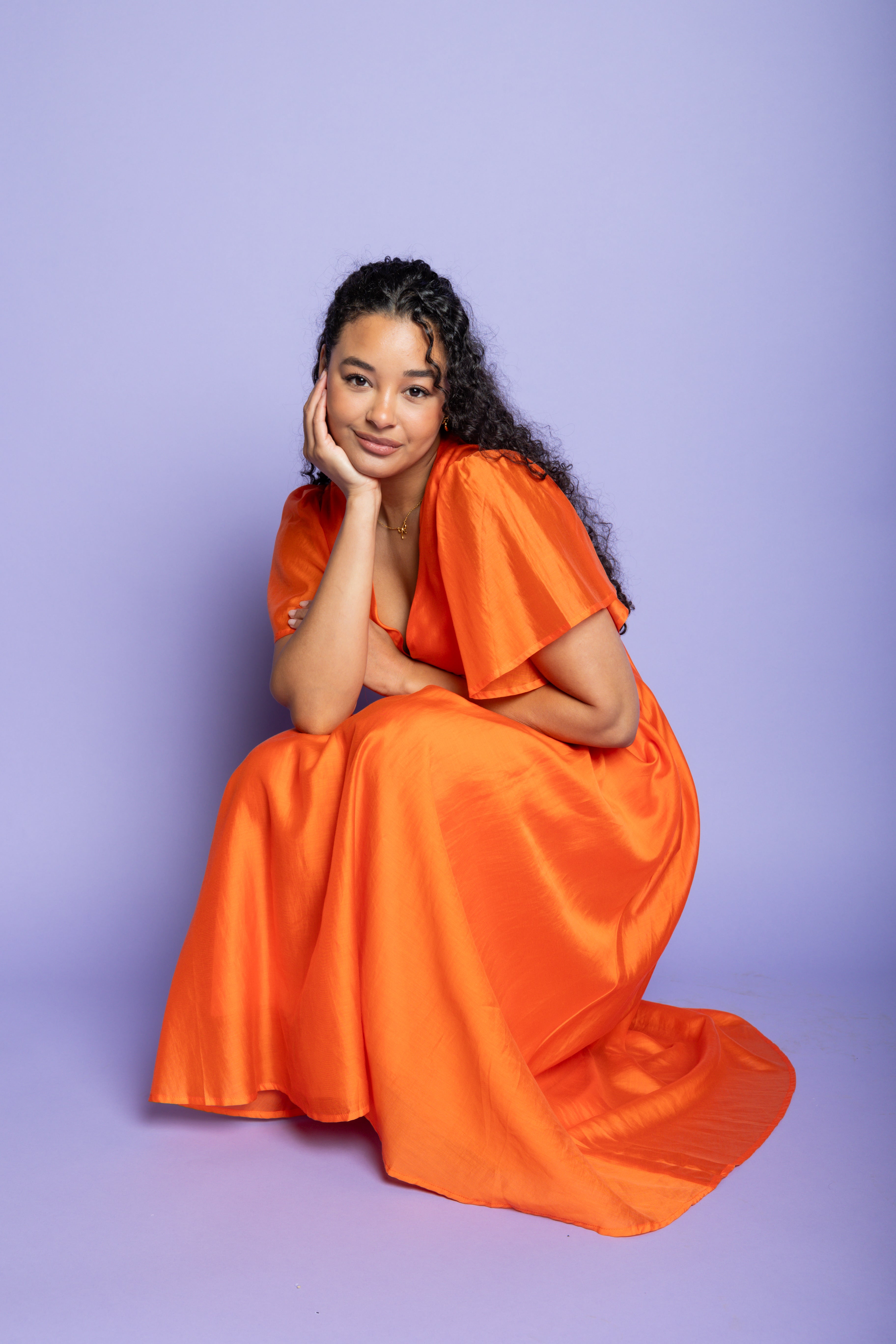 Model in a photoshoot wearing an orange midi dress