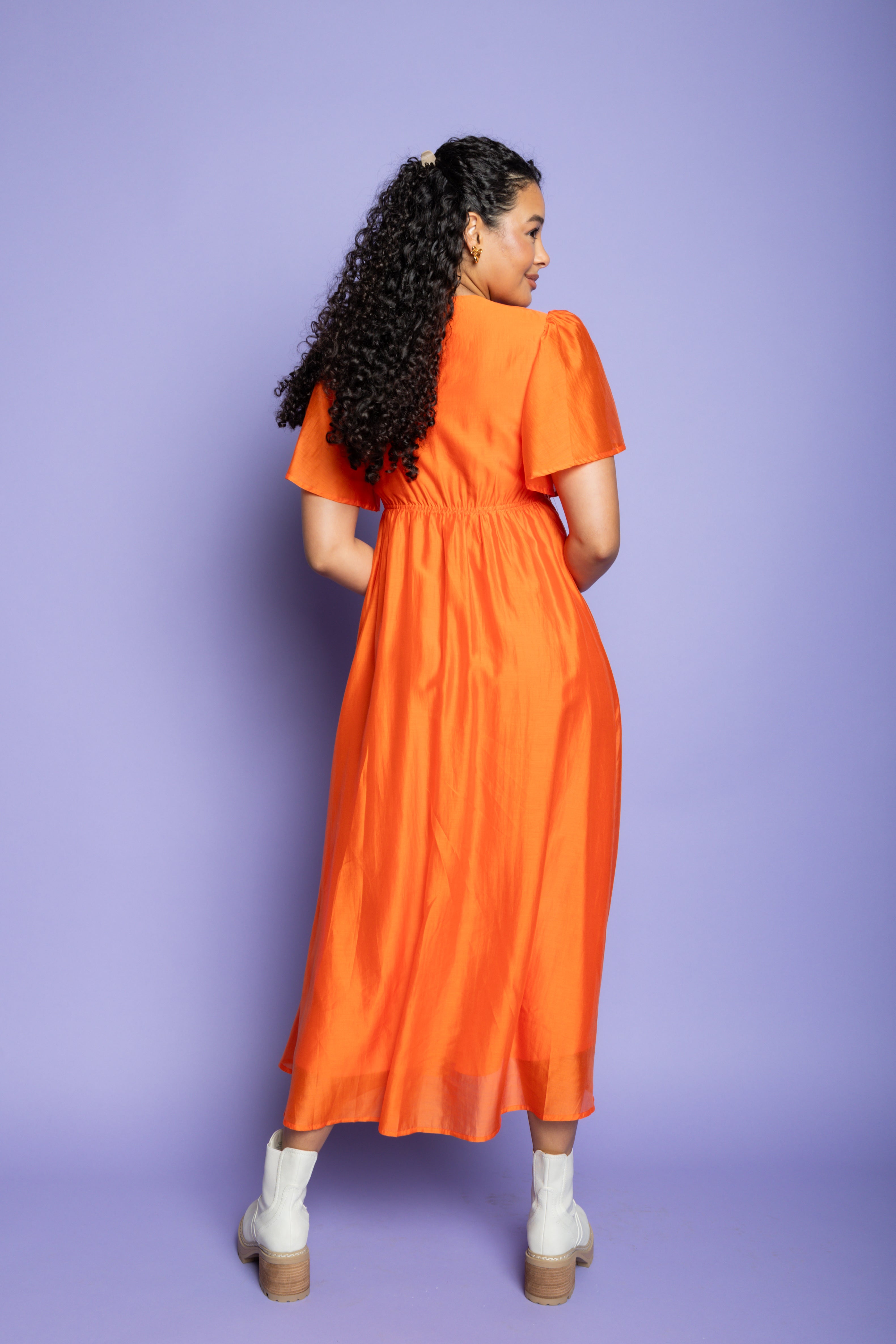 Model in a photoshoot wearing an orange midi dress