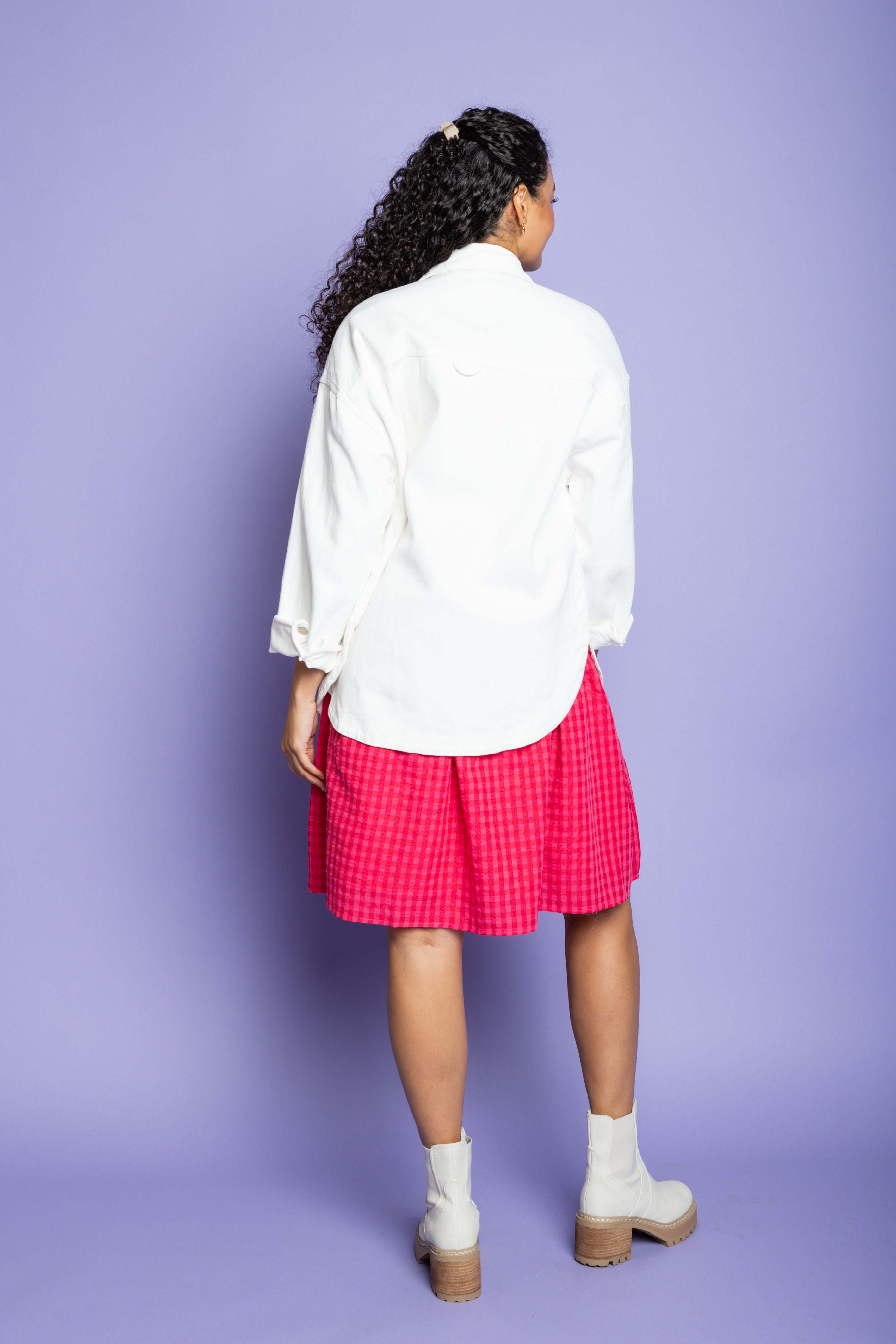 Model is wearing white collared jacket and pink dress.