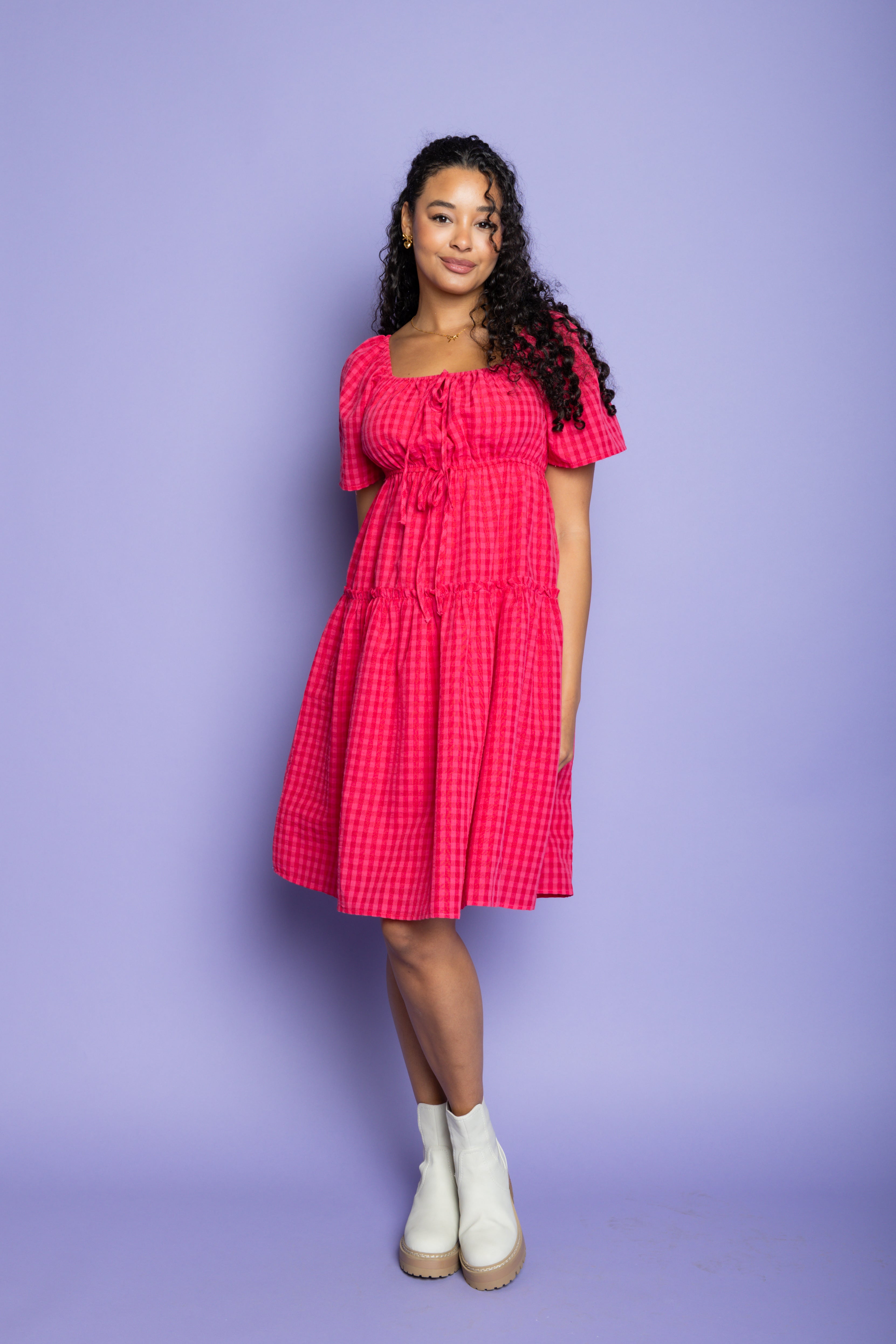 Model wearing pink gingham midi dress and white boots.