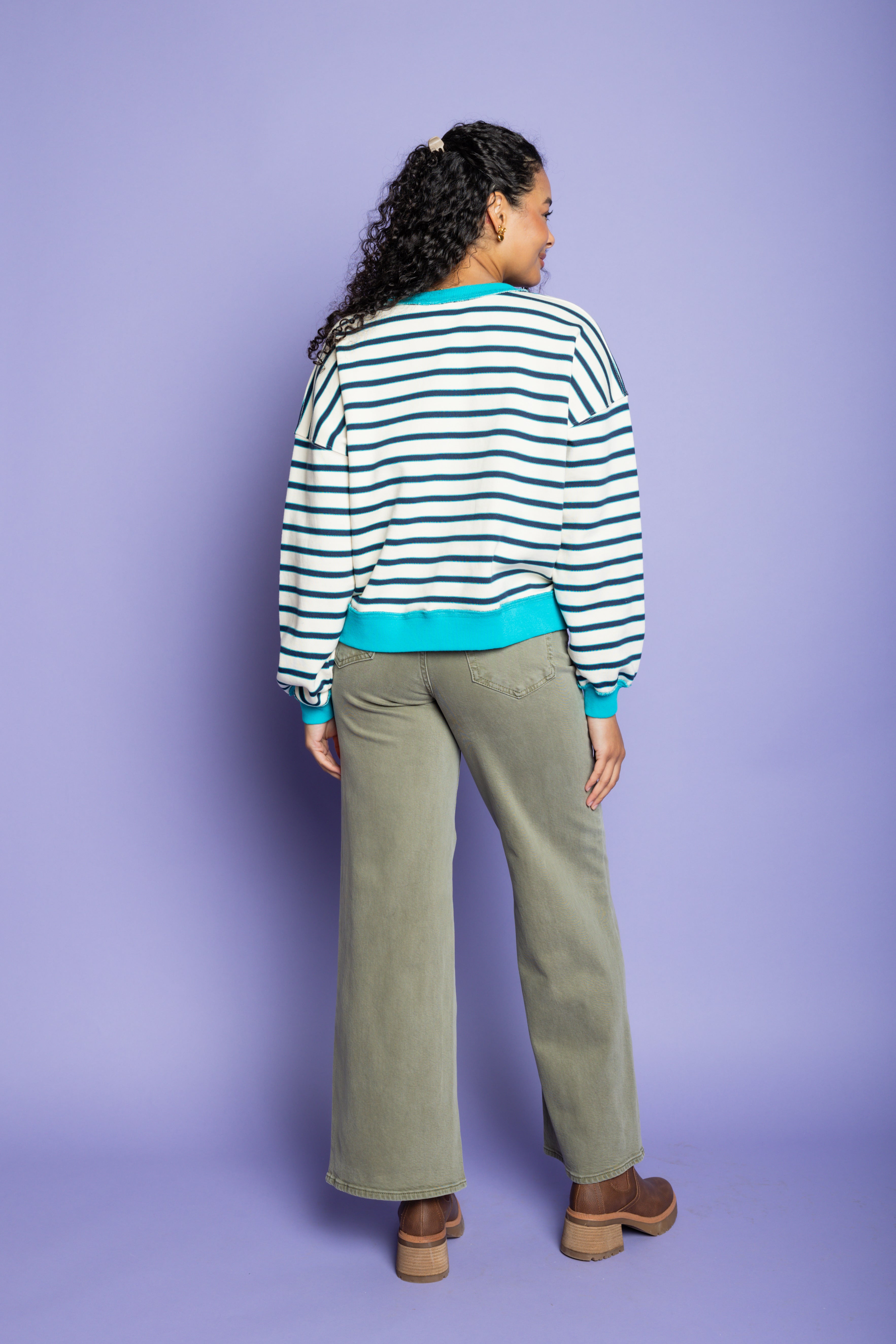 Model is wearing striped oversized top with green pants paired with brown boots 