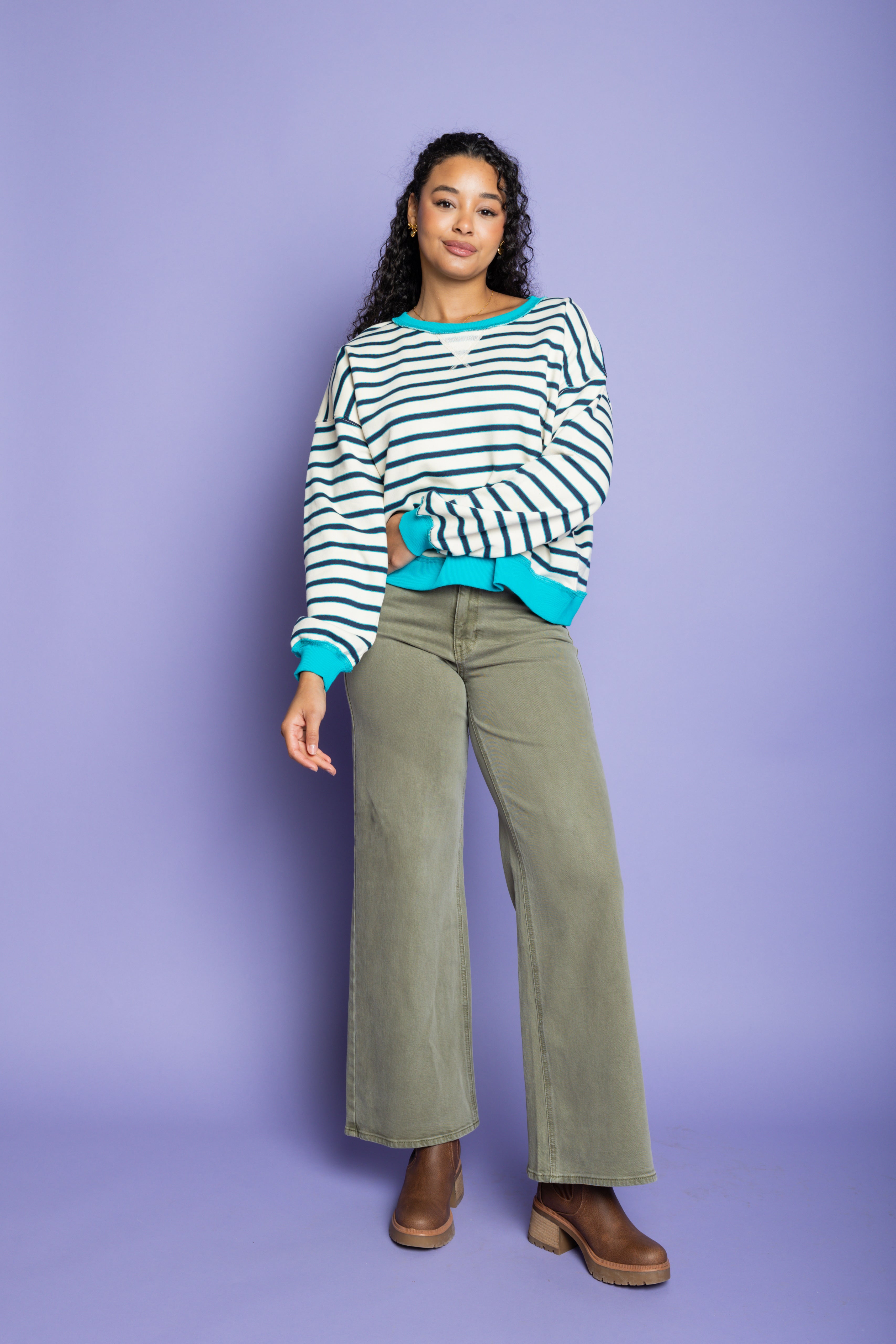 Model is wearing striped oversized top with green pants paired with brown boots 