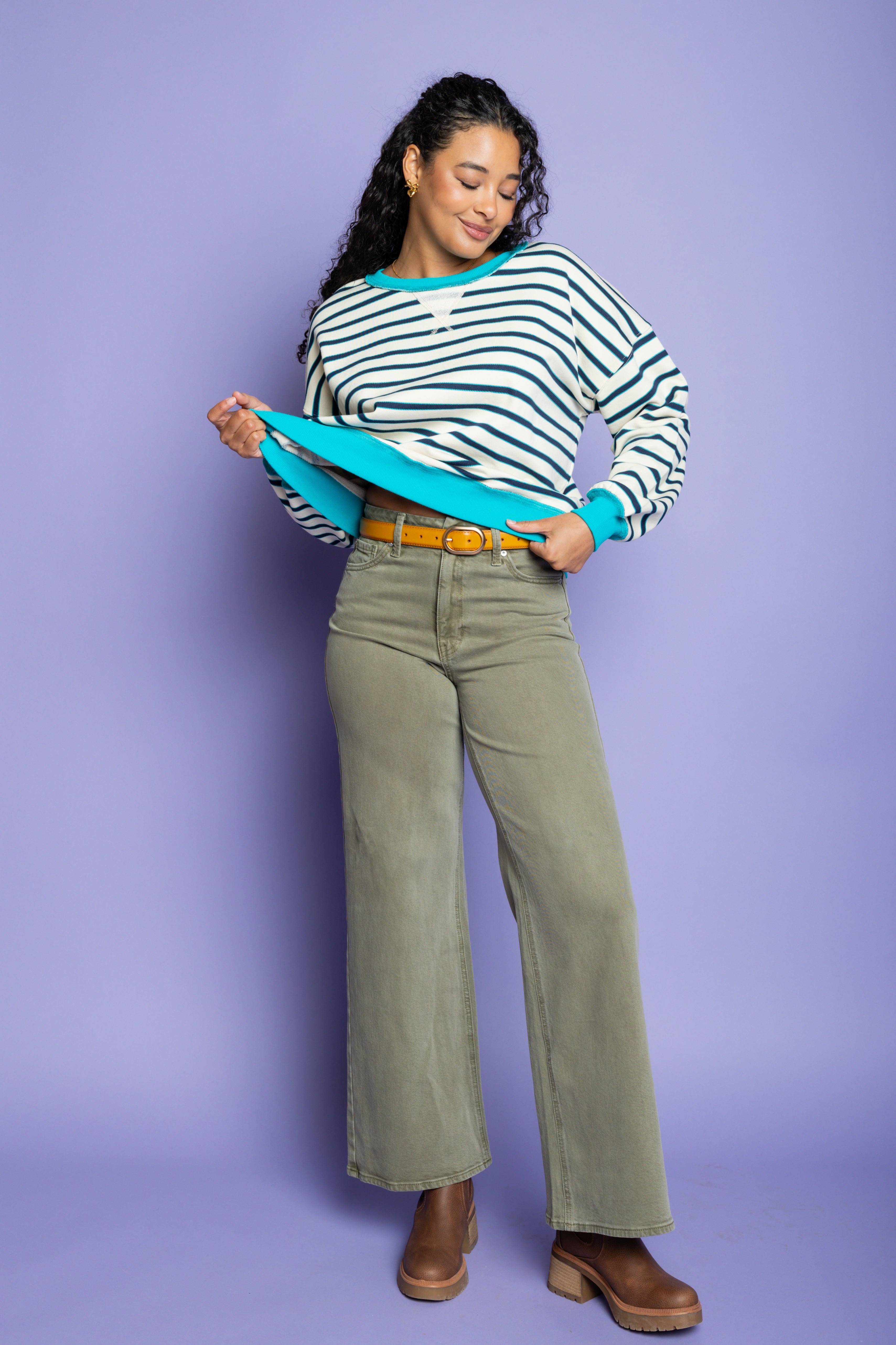 Model is wearing striped oversized top with green pants paired with brown boots 