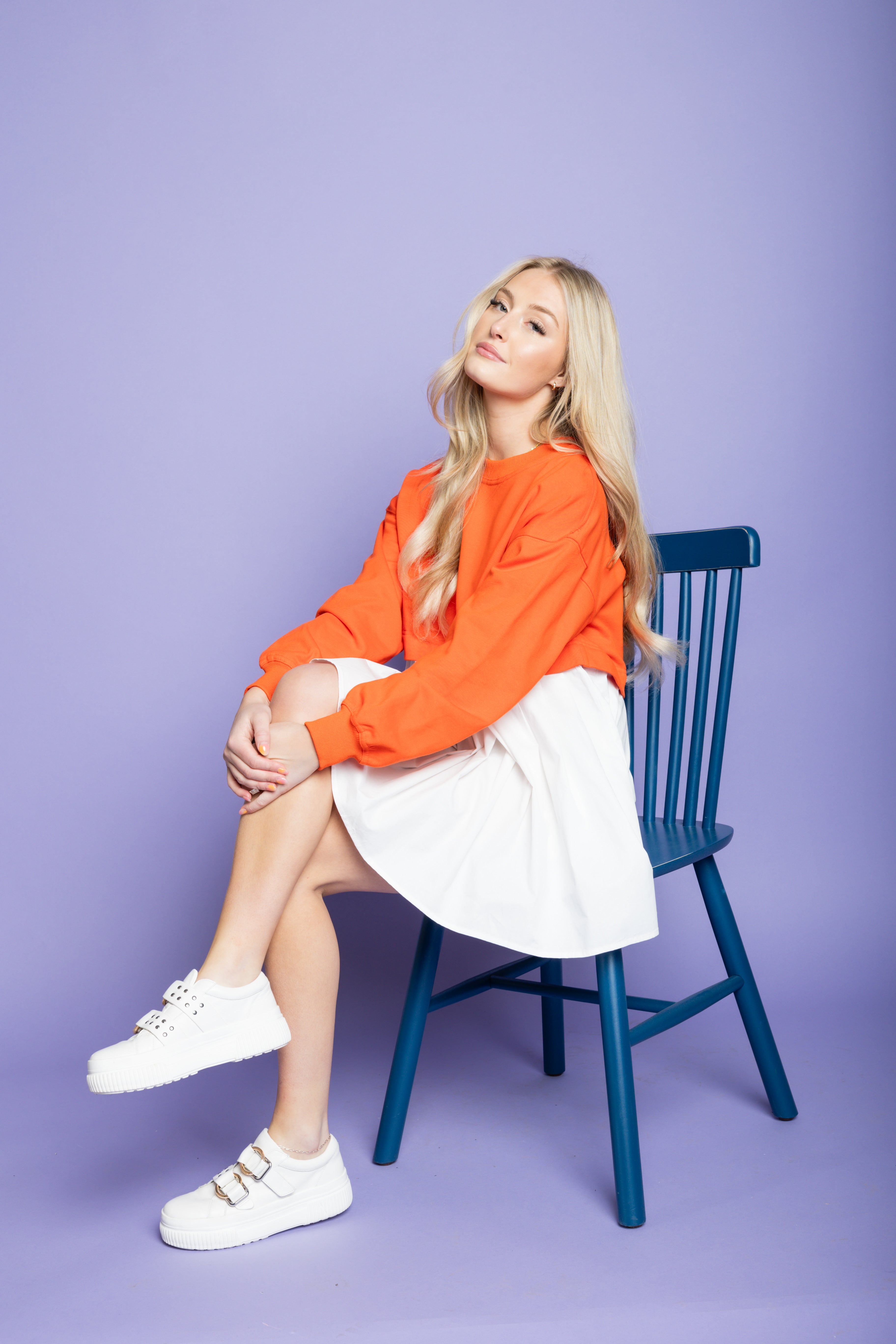 Model is sitting on chair wearing a mini orange and white chair. 