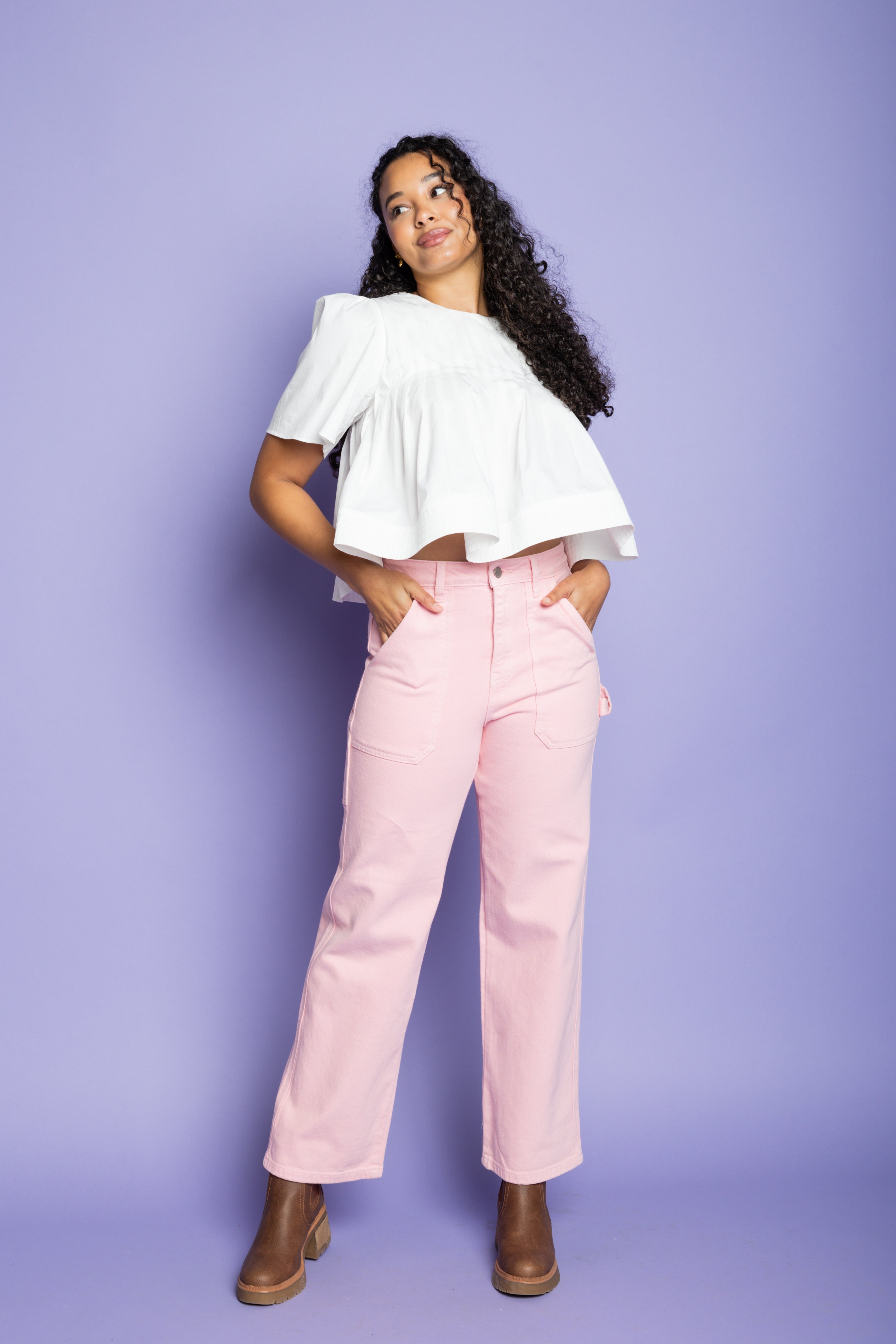 Model is wearing a short sleeve white blouse and pink cargo pants with brown boots.