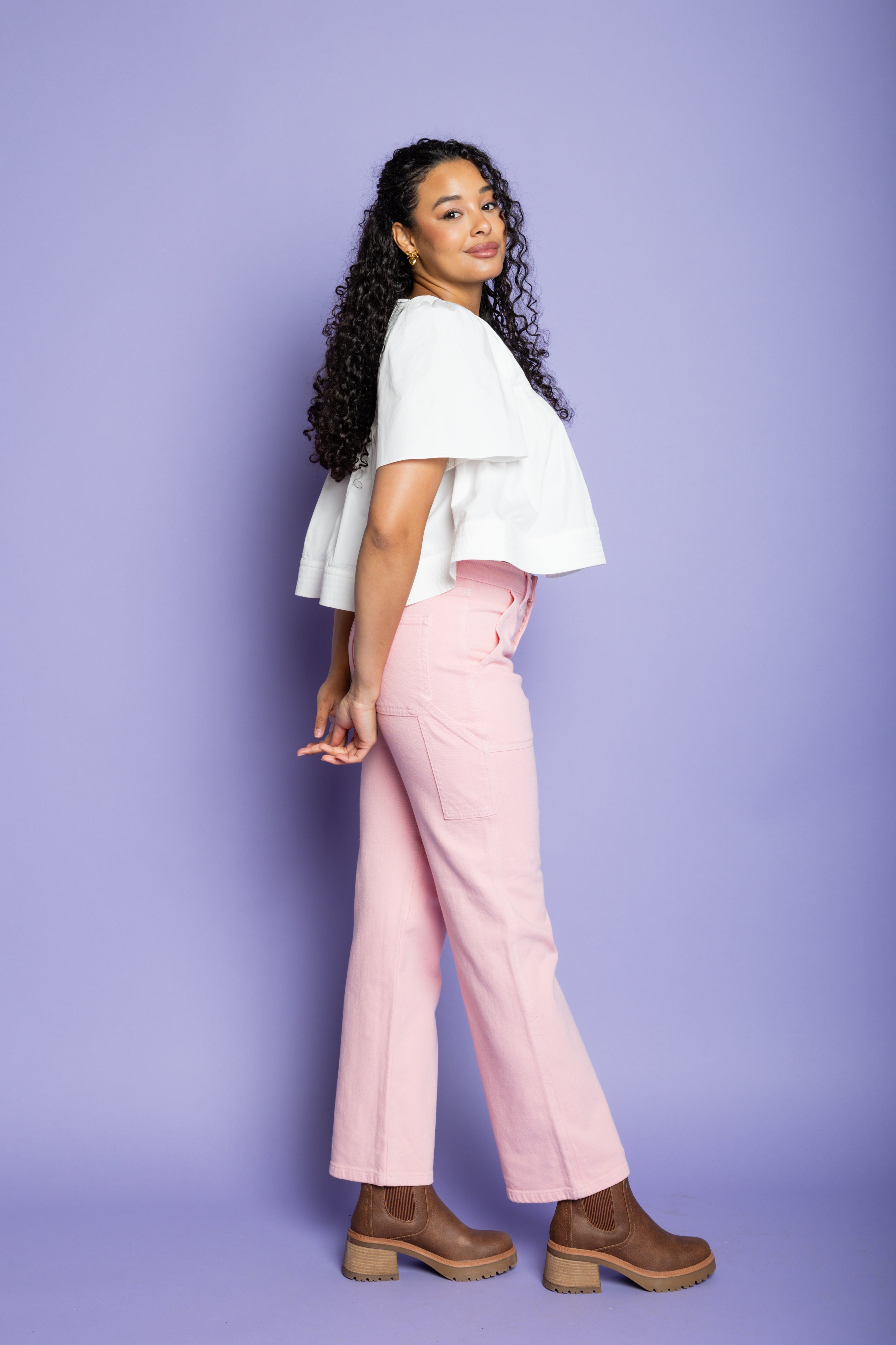 Model is wearing a short sleeve white blouse and pink cargo pants with brown boots.