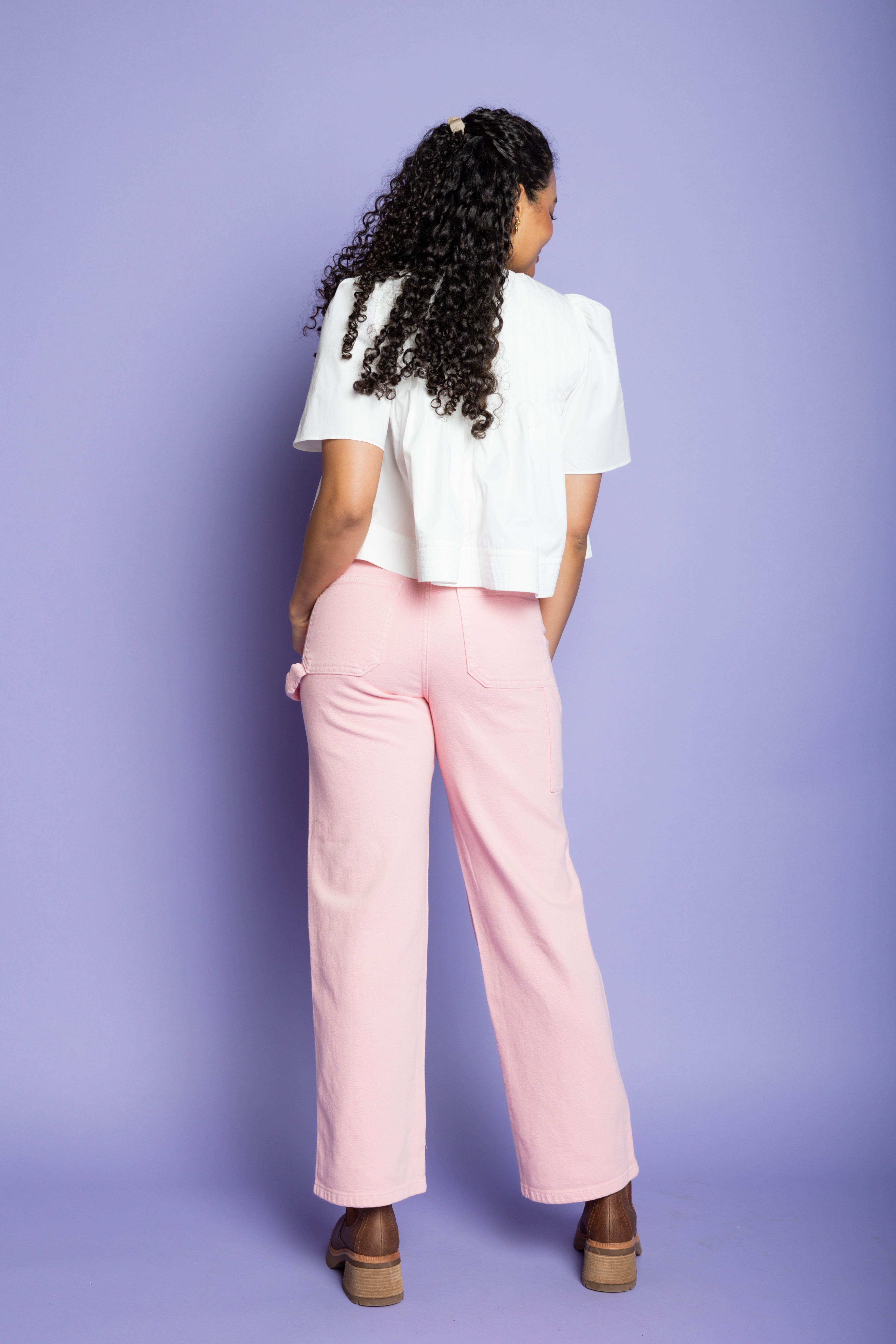 Model is wearing a short sleeve white blouse and pink cargo pants with brown boots.