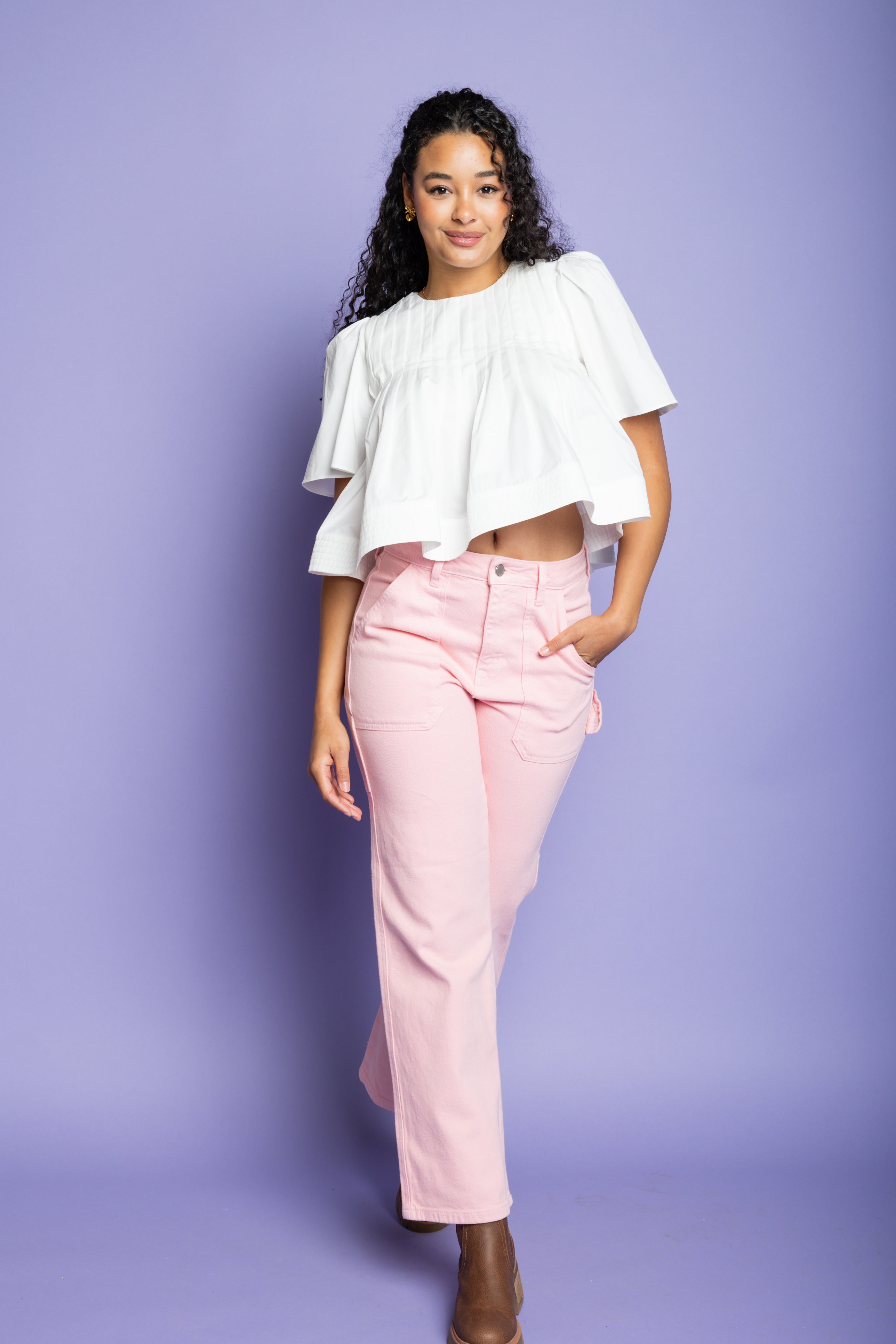 Model is wearing a short sleeve white blouse and pink cargo pants with brown boots.