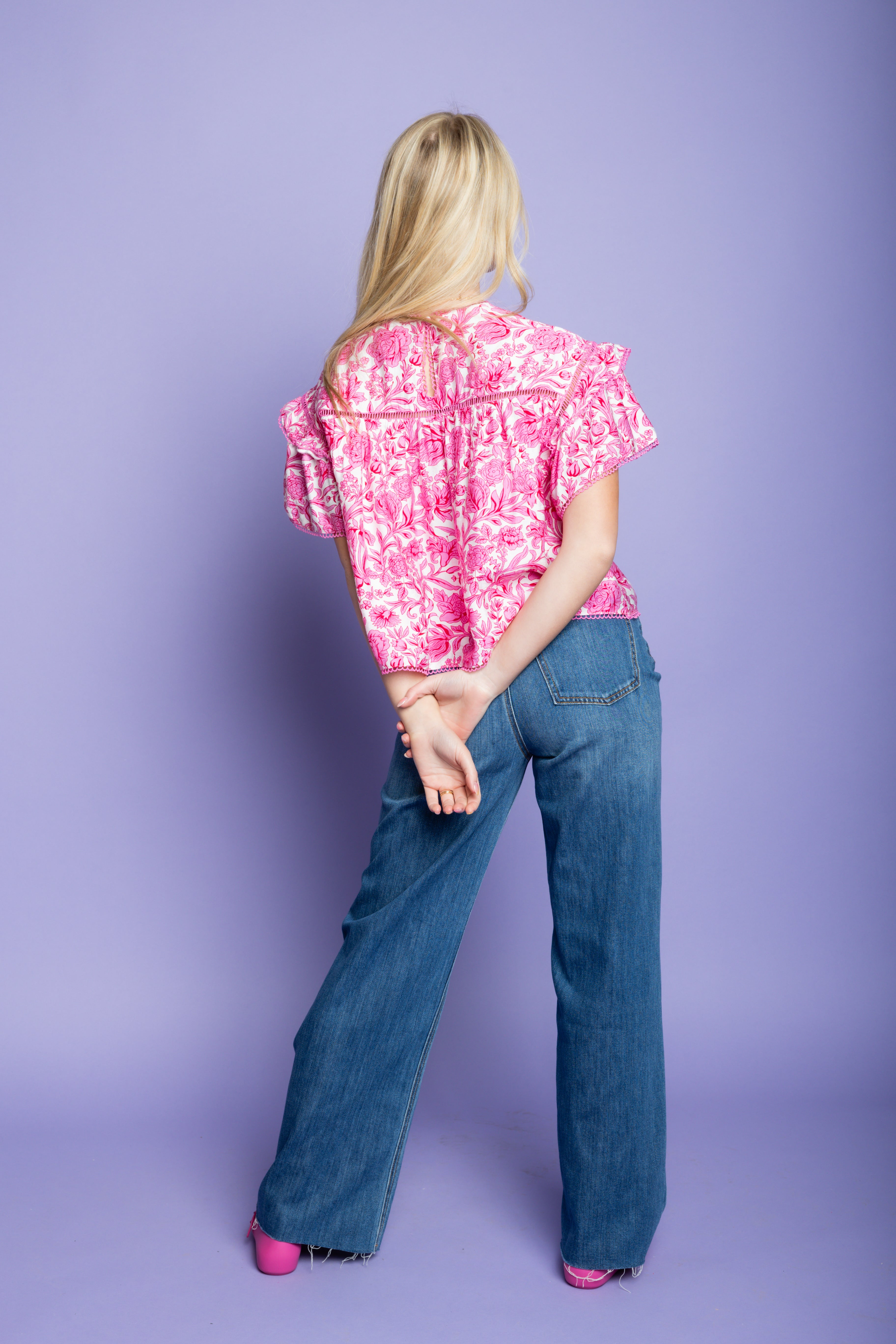 Model is wearing a puff sleeve pink floral shirt with medium wash denim jeans.