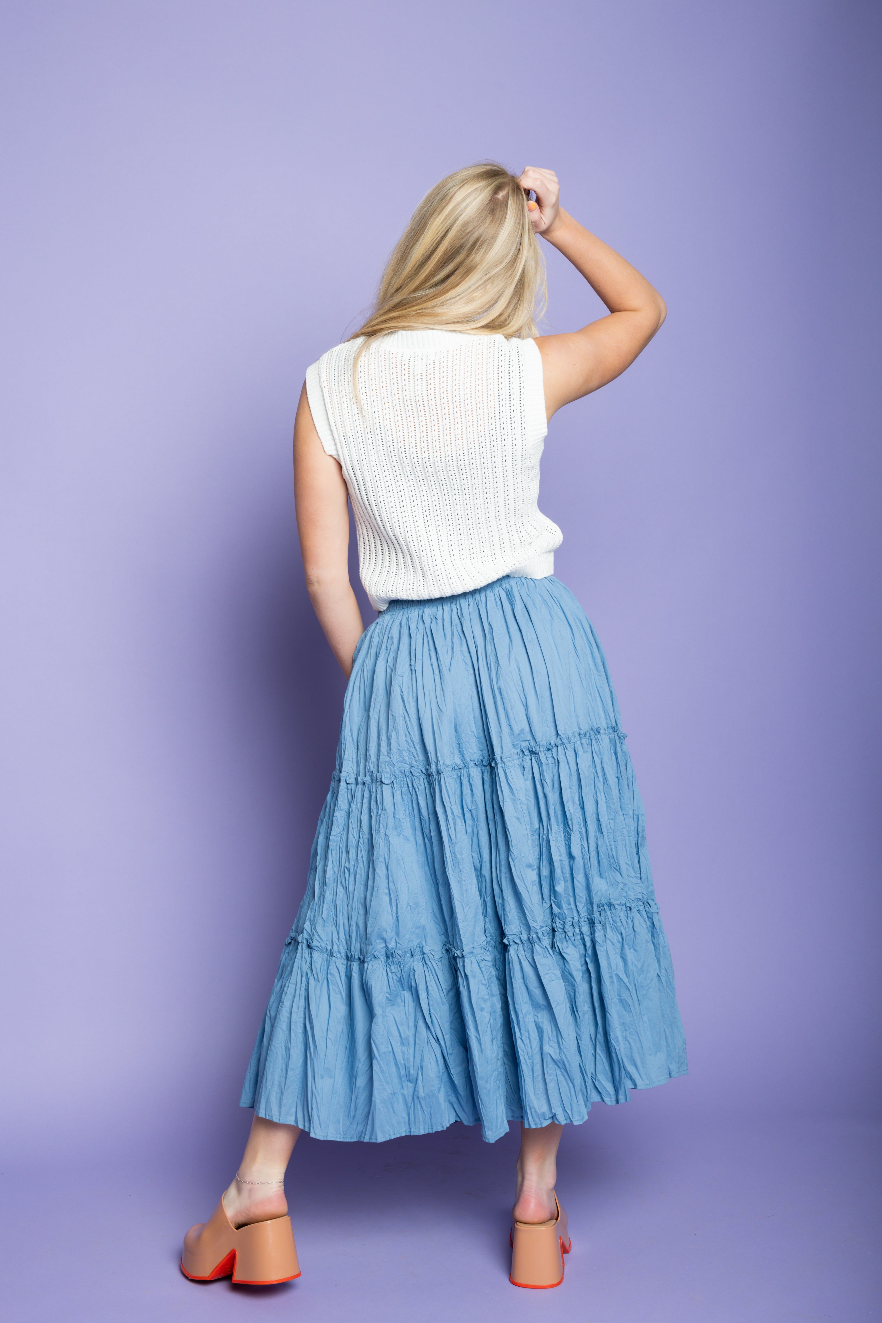 Model is wearing white tank sweater vest and blue midi skirt.