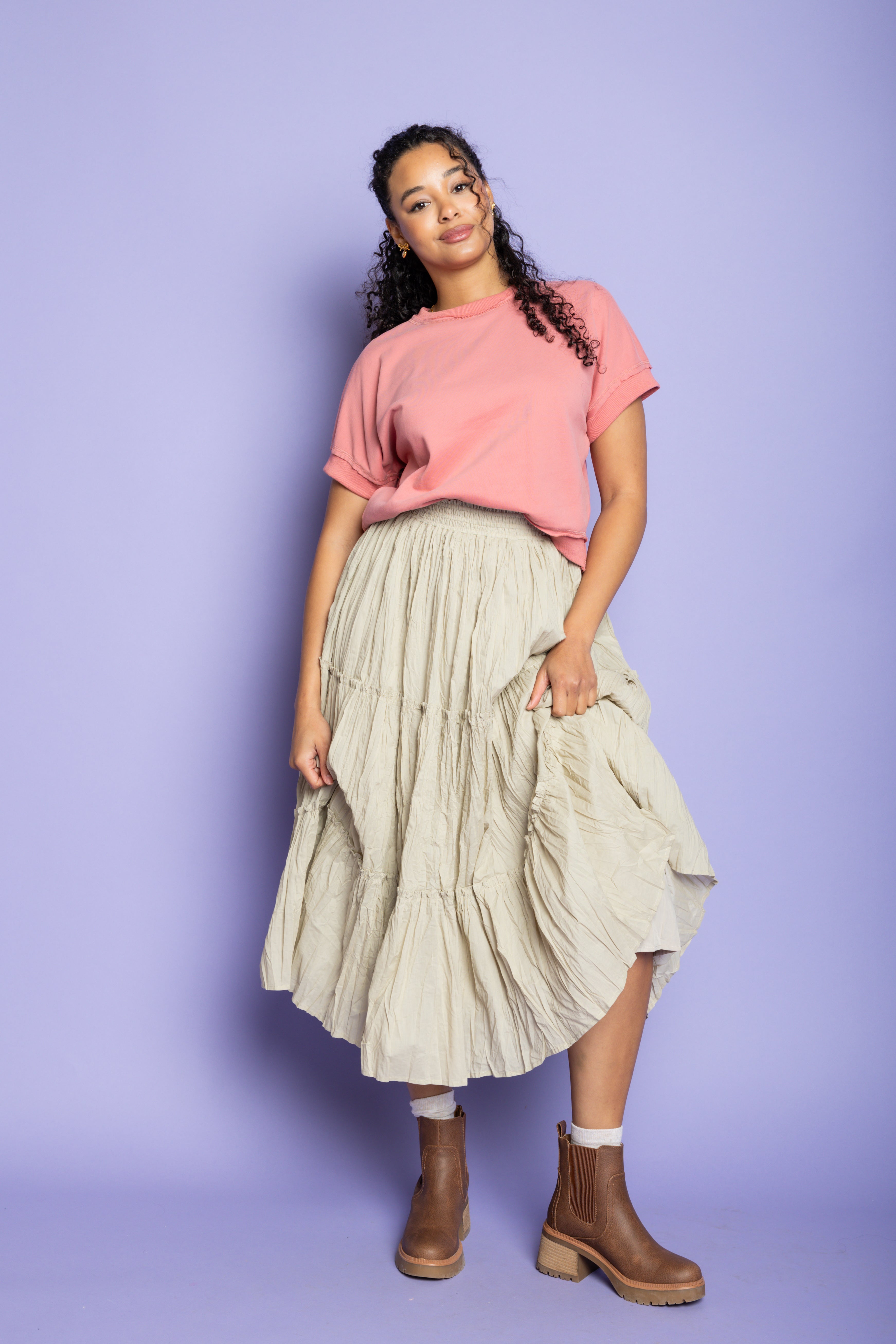 Model is wearing a pink t-shirt with tan ruffle skirt and brown boots.