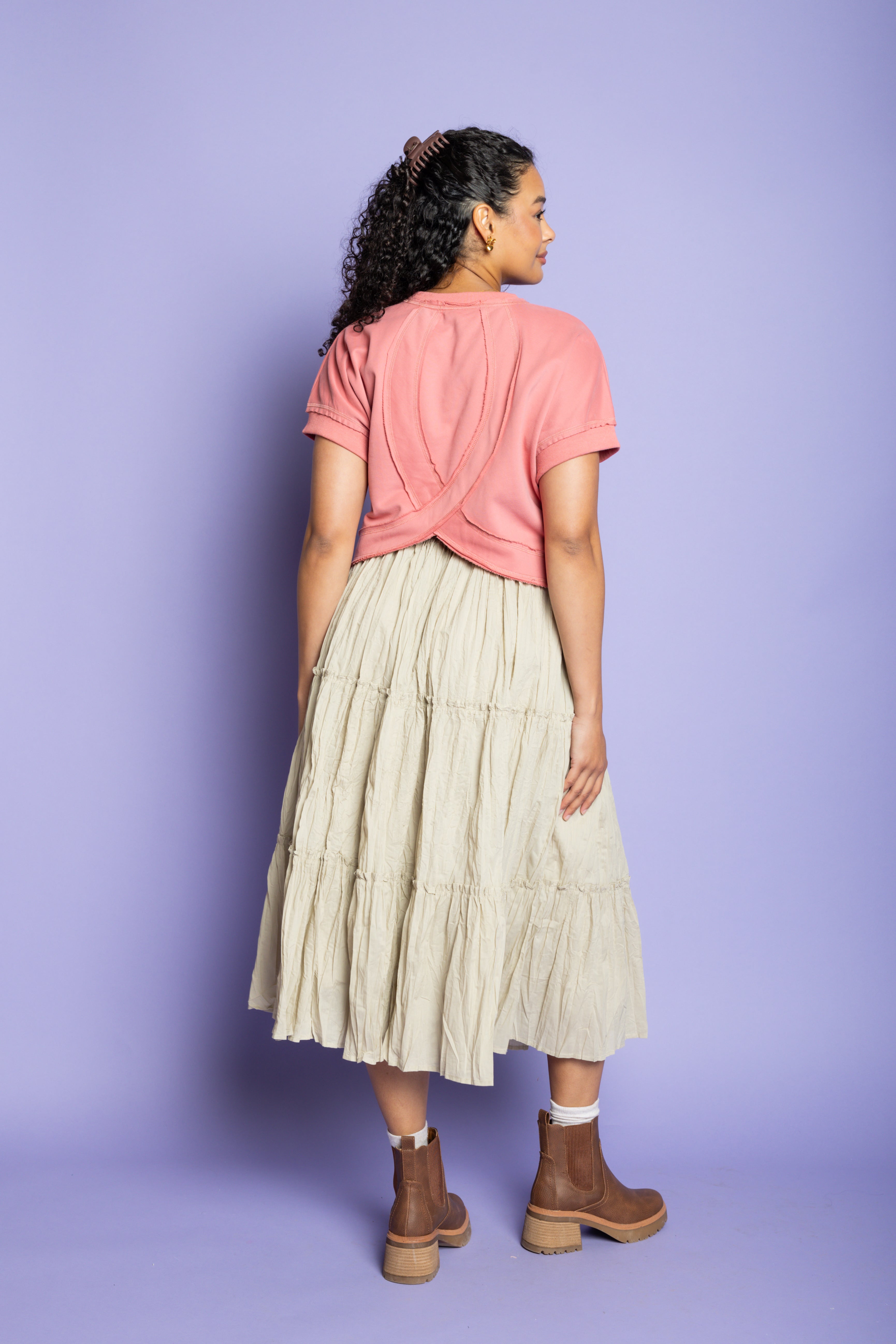 Model is wearing a pink t-shirt with tan ruffle skirt and brown boots.