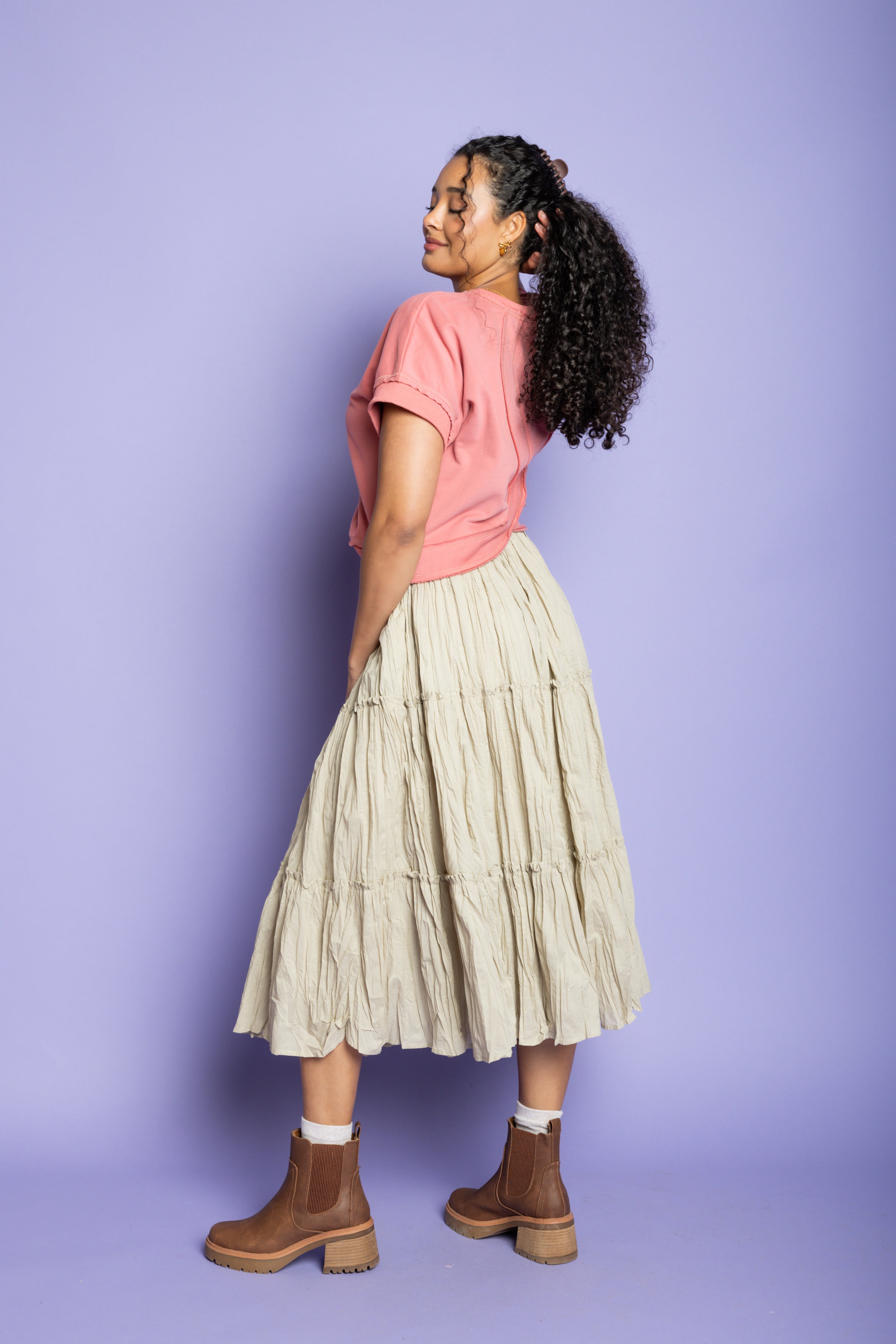 Model is wearing a pink t-shirt with tan ruffle skirt and brown boots.