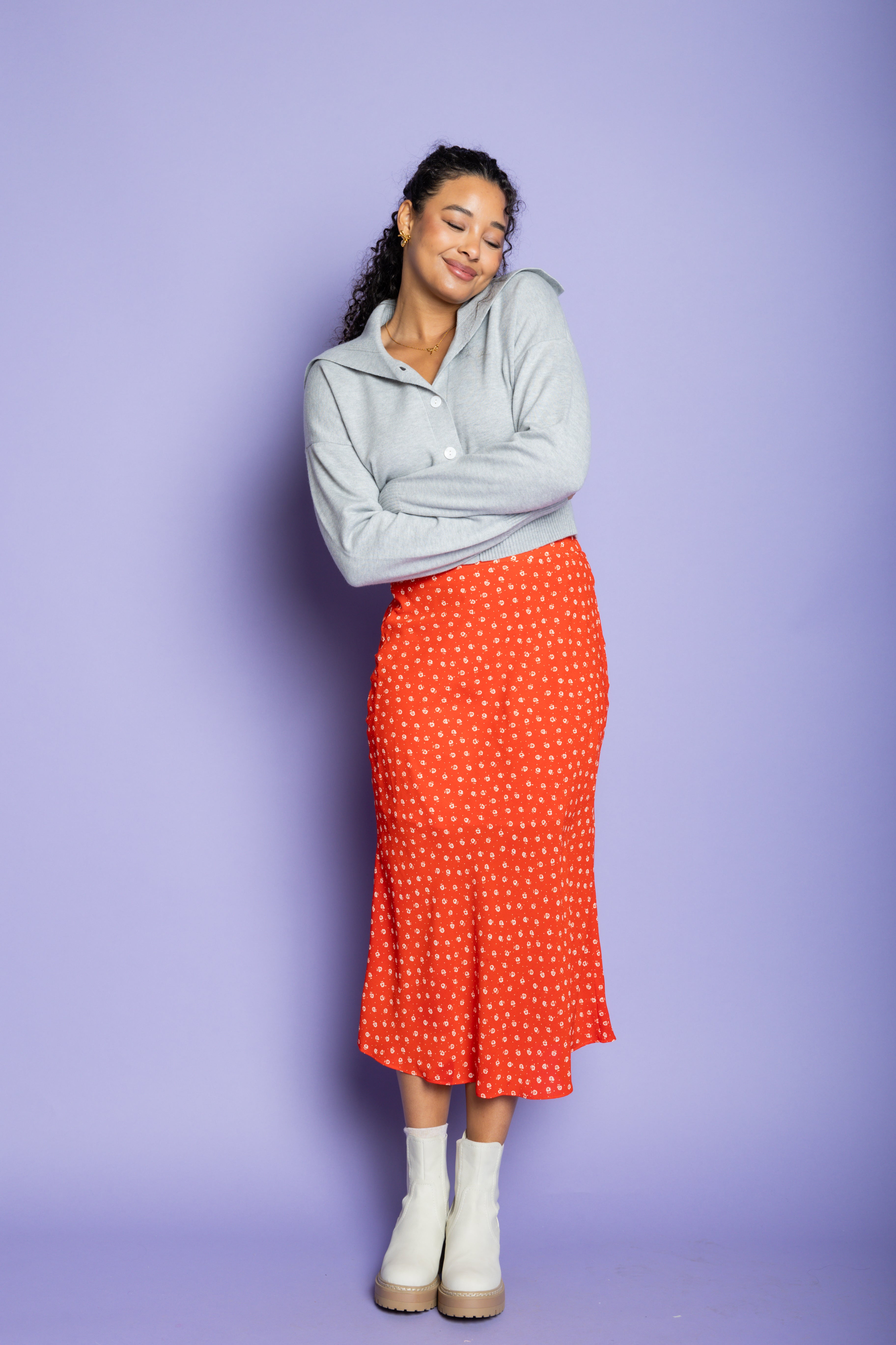 Model is wearing a grey cardigan and red midi skirt.