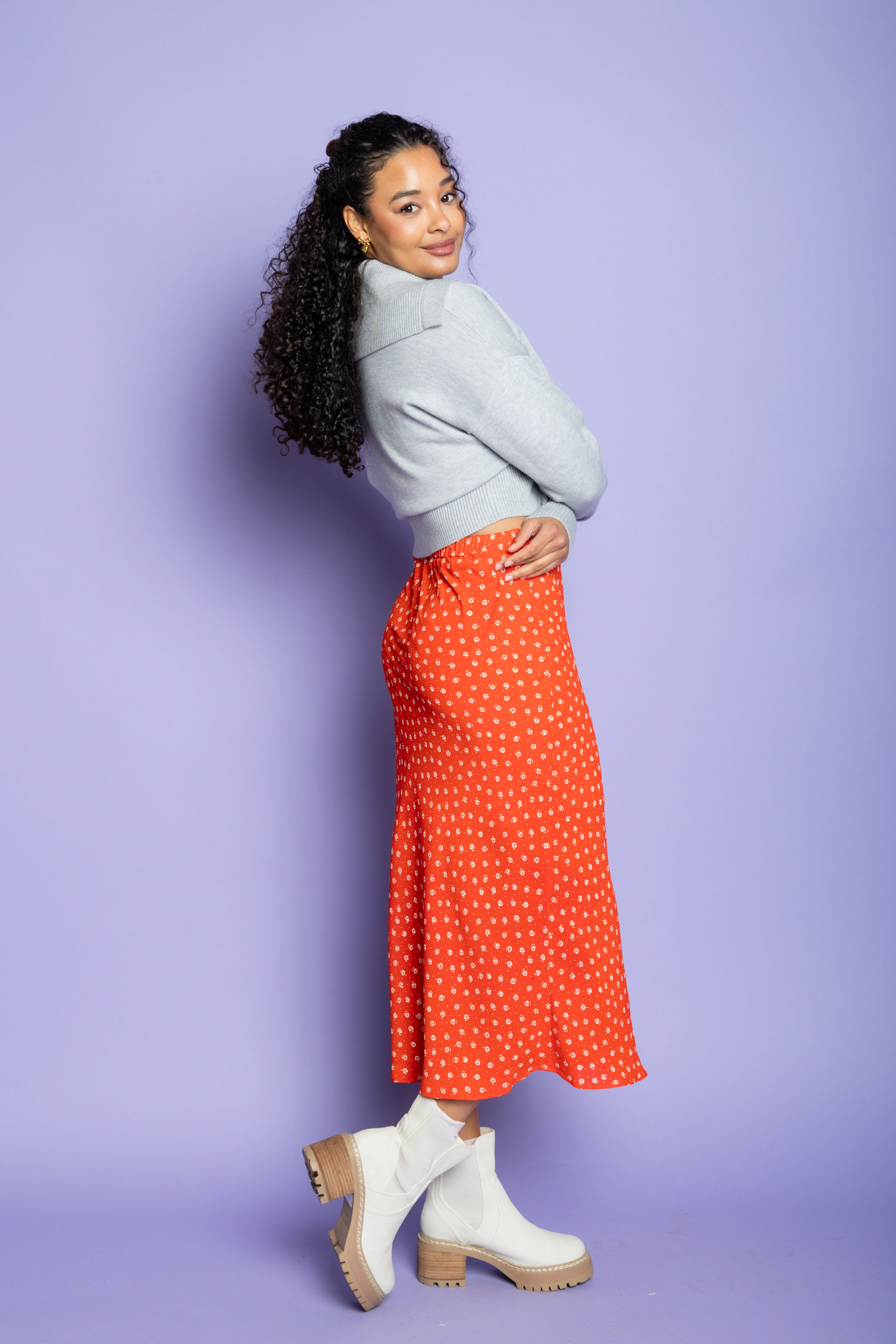 Model is wearing grey cardigan and orange skirt.