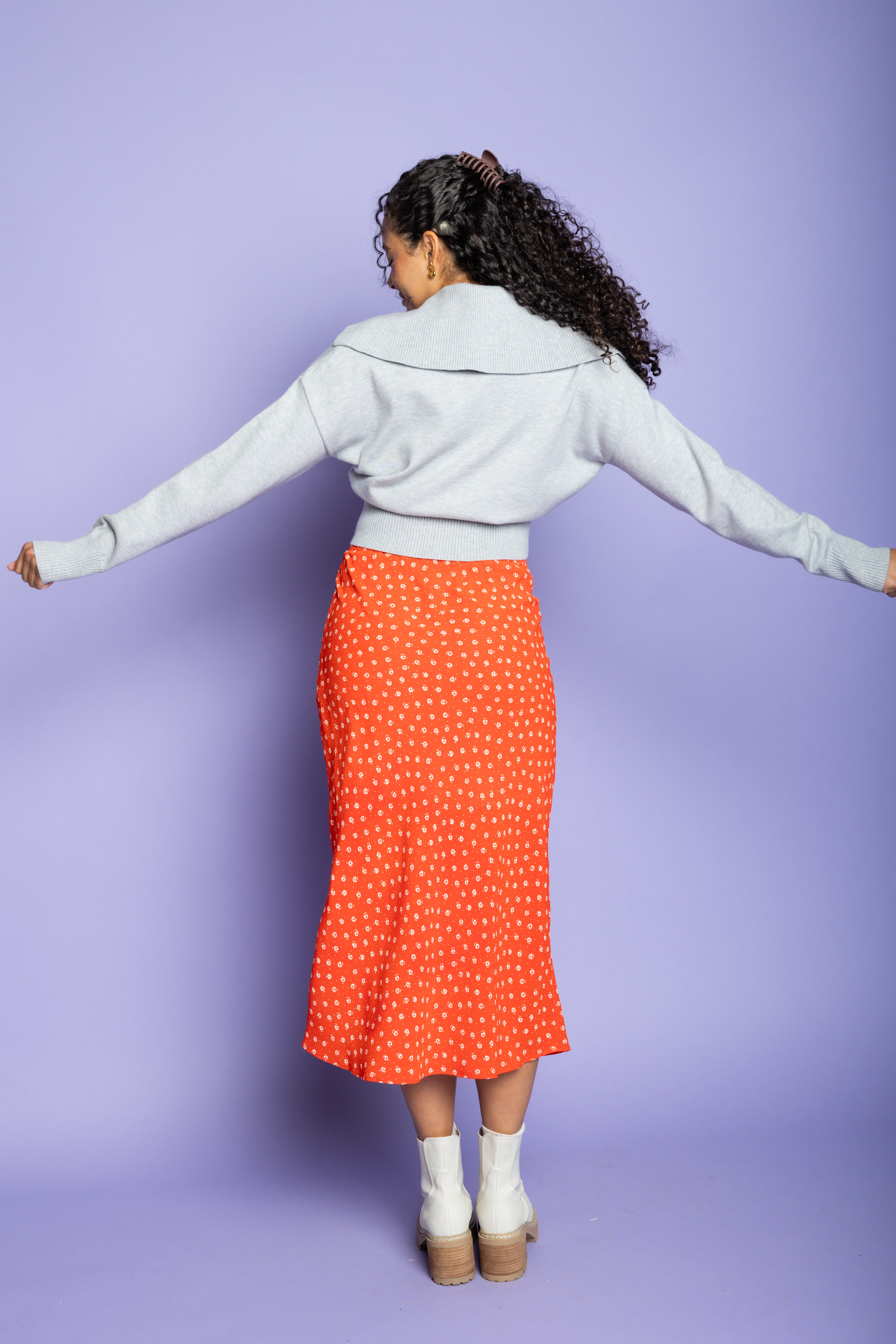 Model is wearing grey cardigan and orange skirt.