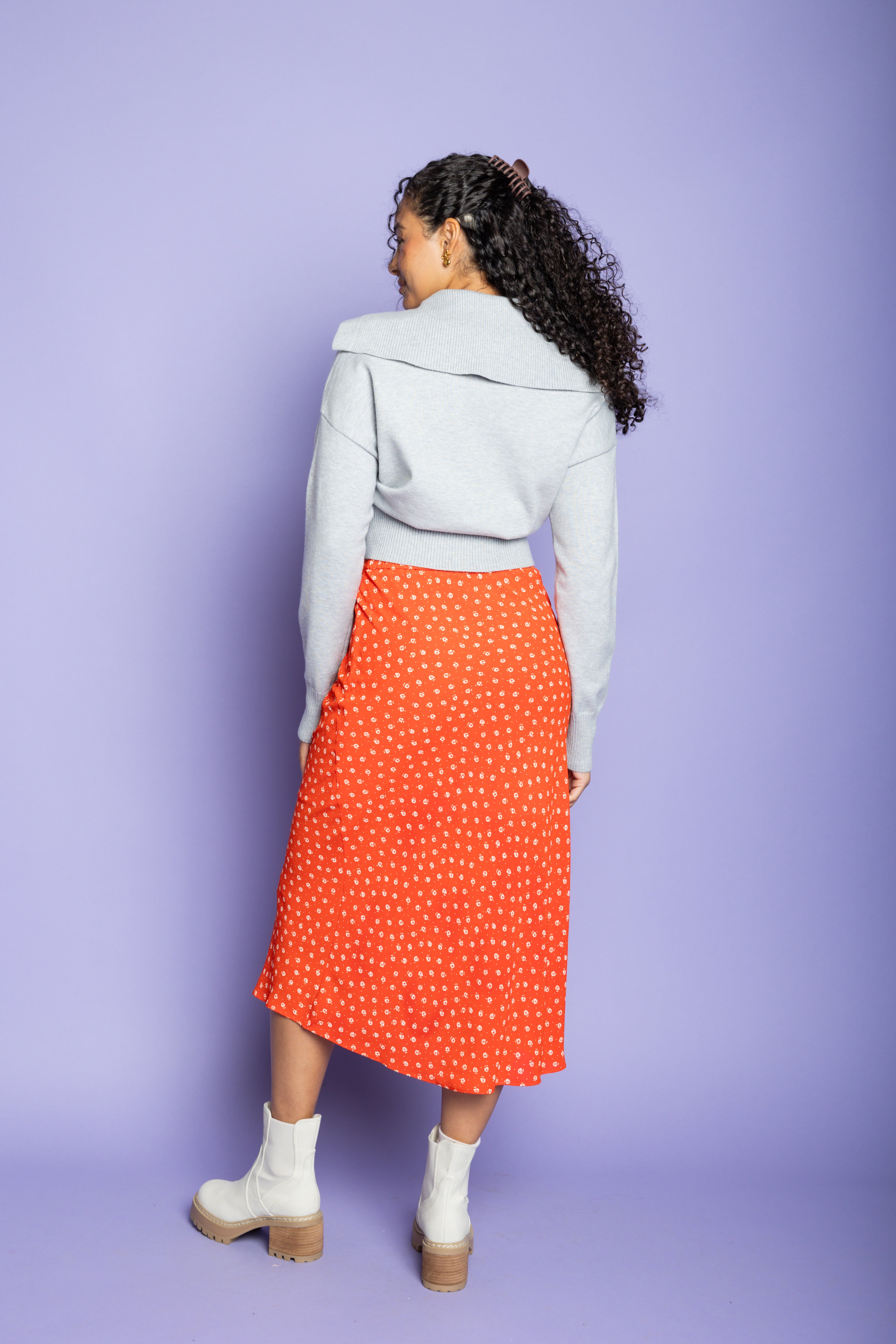 Model is wearing a grey cardigan and red midi skirt.