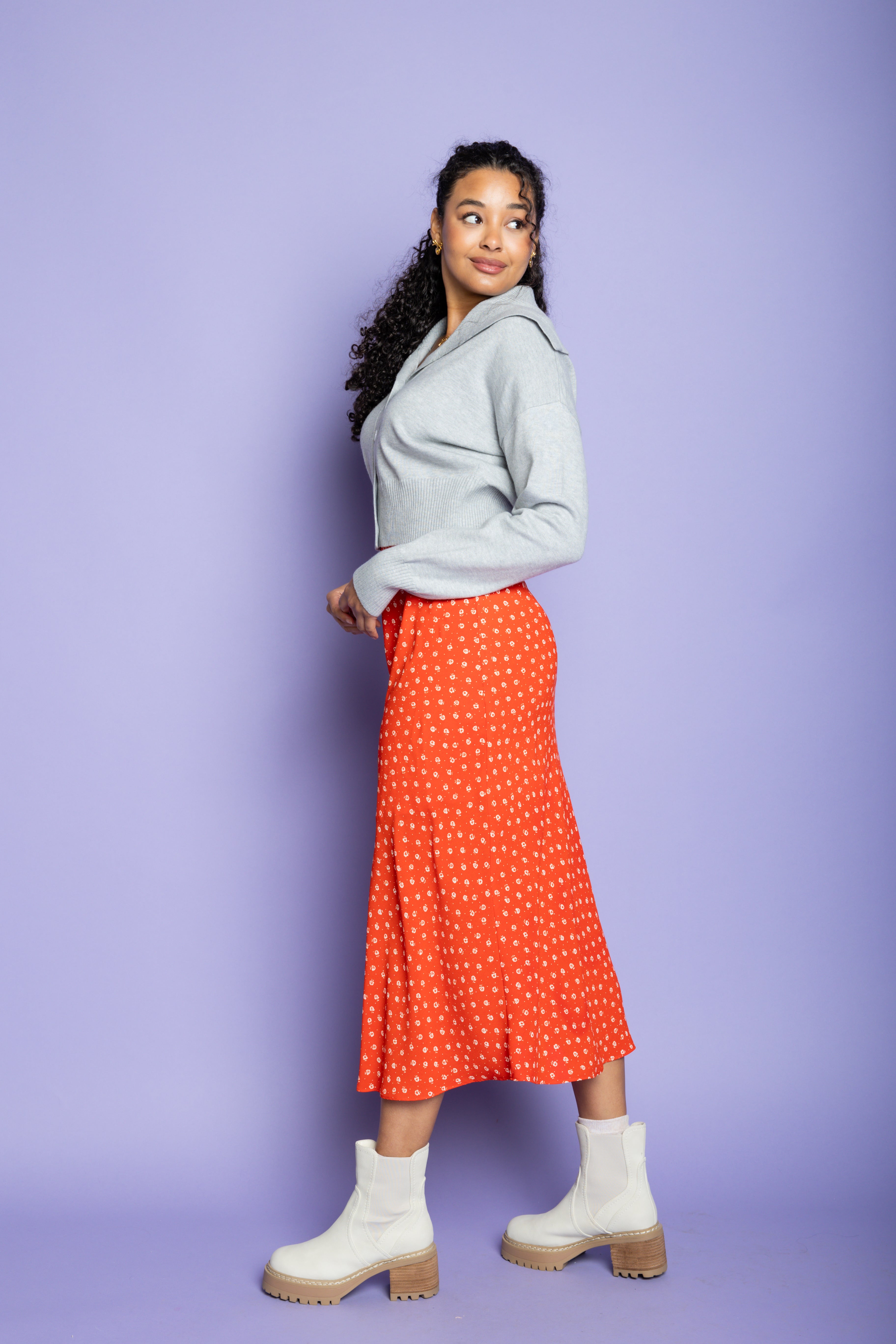 Model is wearing a grey cardigan and red midi skirt.