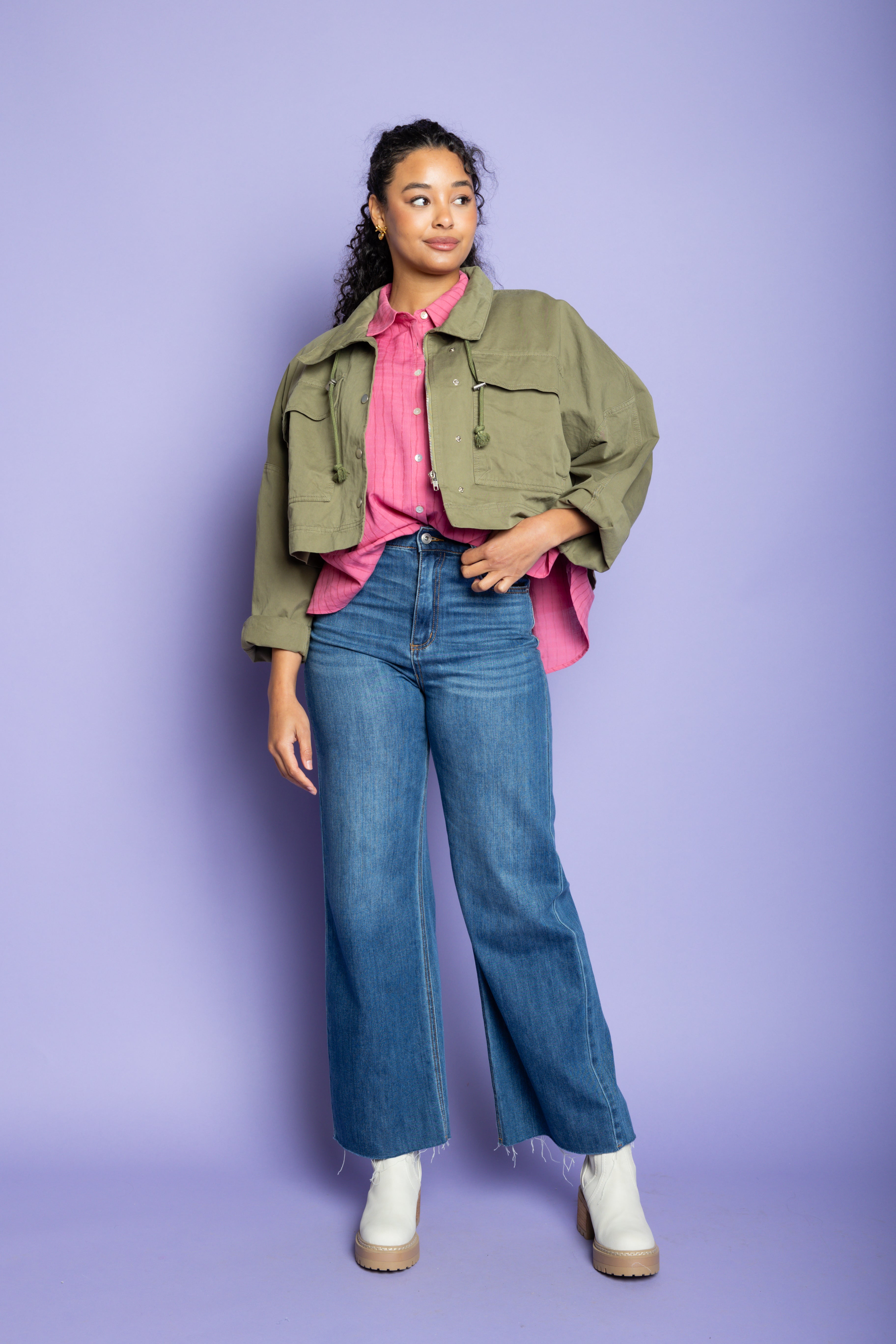 Model wearing a green jacket with pink button up and blue jeans.