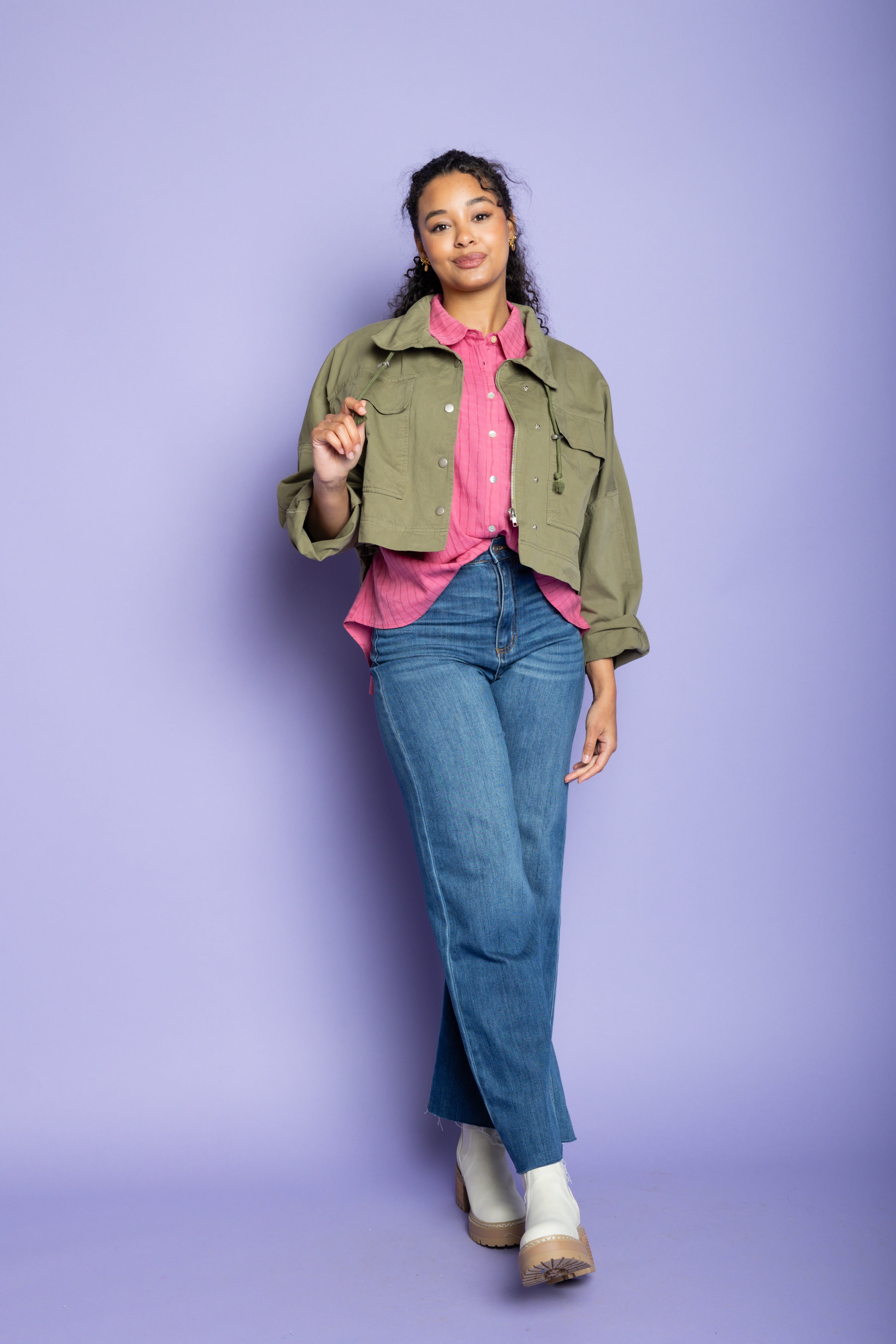 Model wearing a green jacket with pink button up and blue jeans.