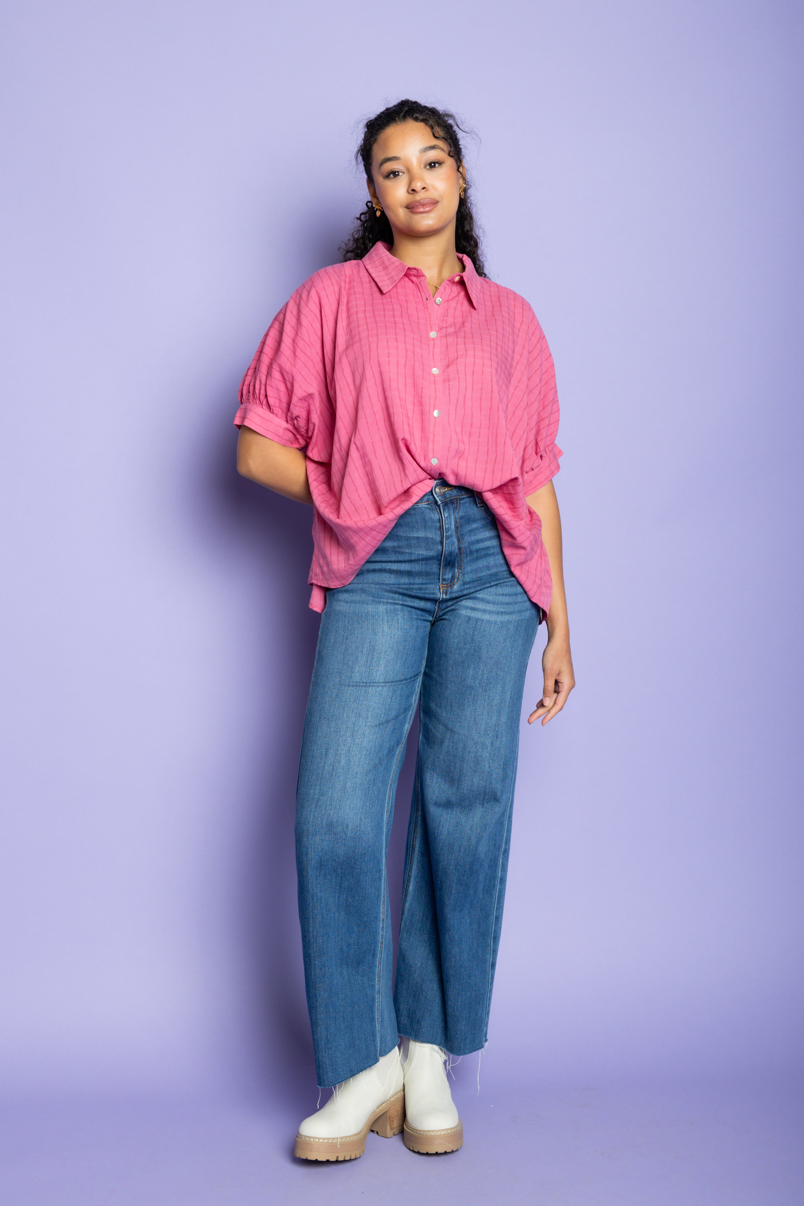 Model wearing pink oversized blouse with blue jeans and boots.