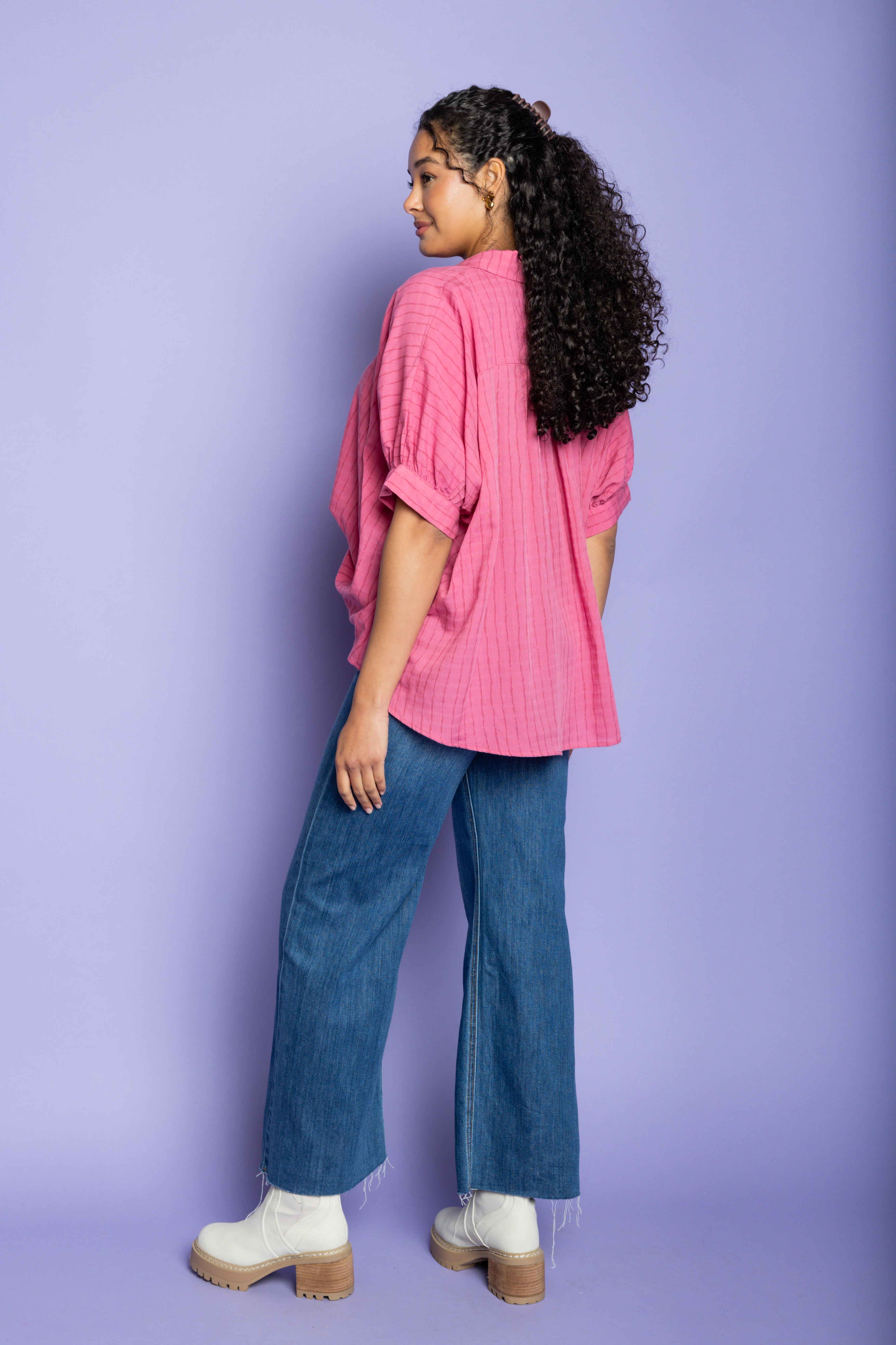 Model wearing pink oversized blouse with blue jeans and boots.