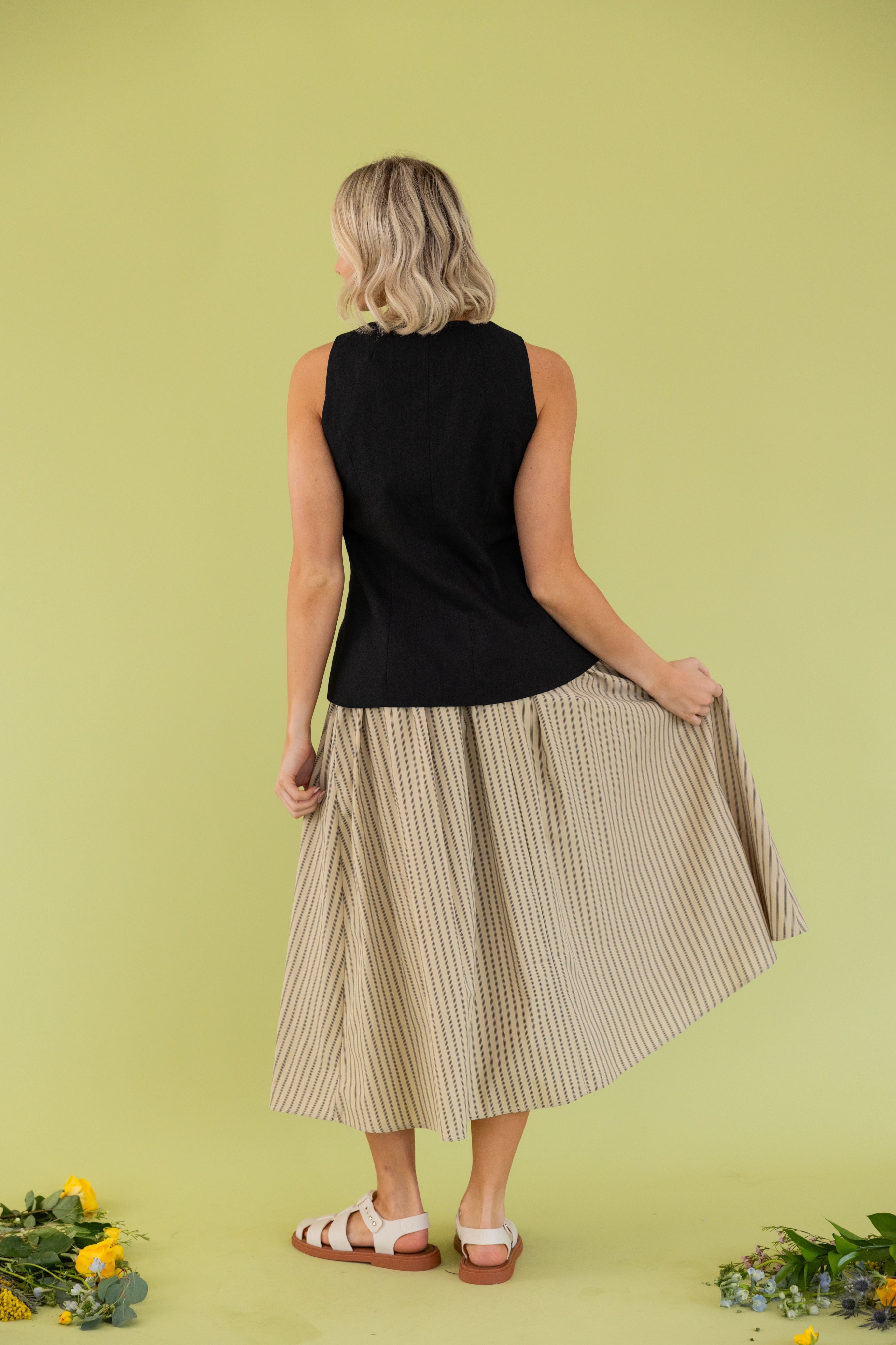 Model is wearing black vest with smocked tan striped midi skirt.