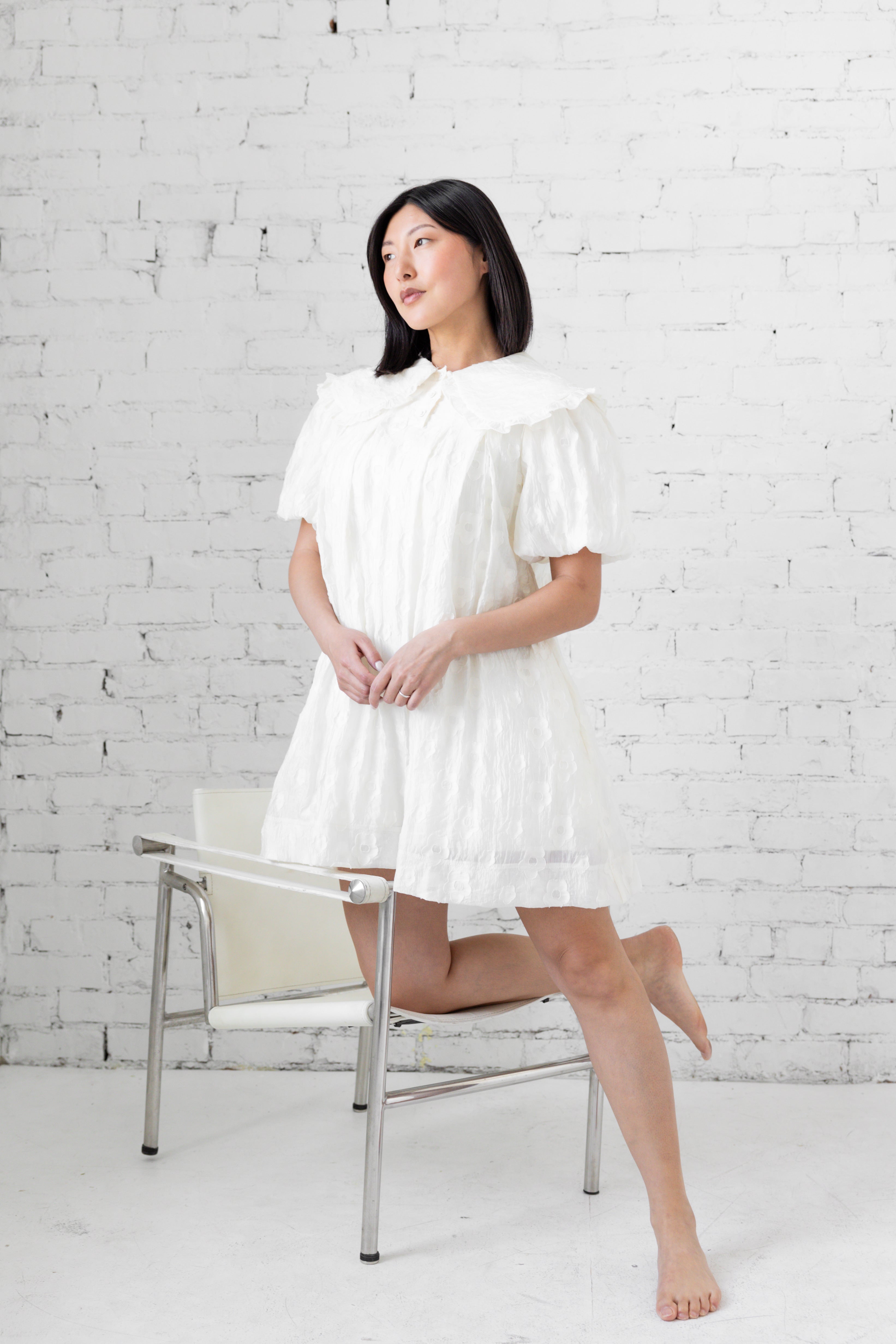 Model wearing white mini dress with puffer sleeves and peter pan collar.
