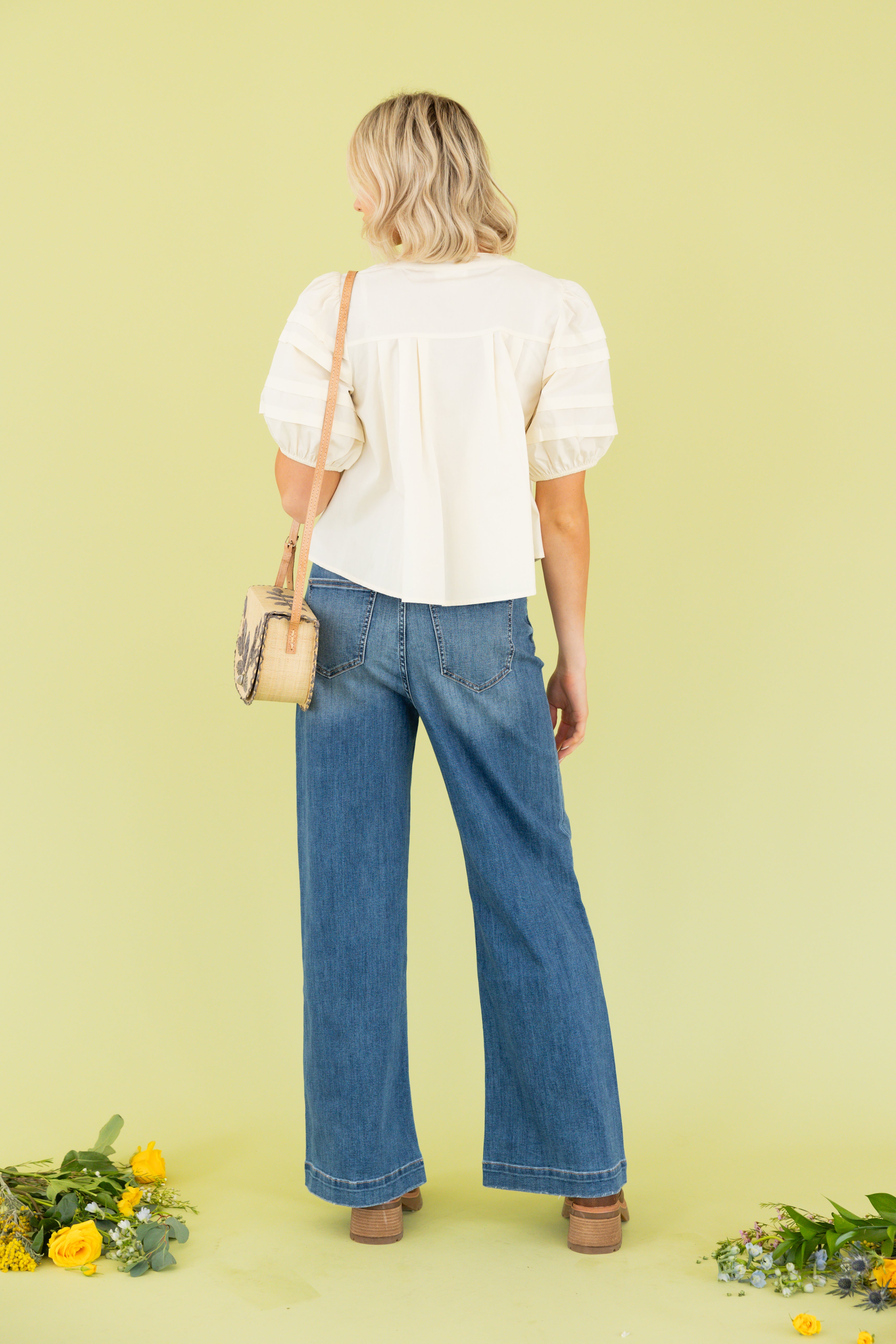 Model is wearing white blouse with wide leg dark wash jean 